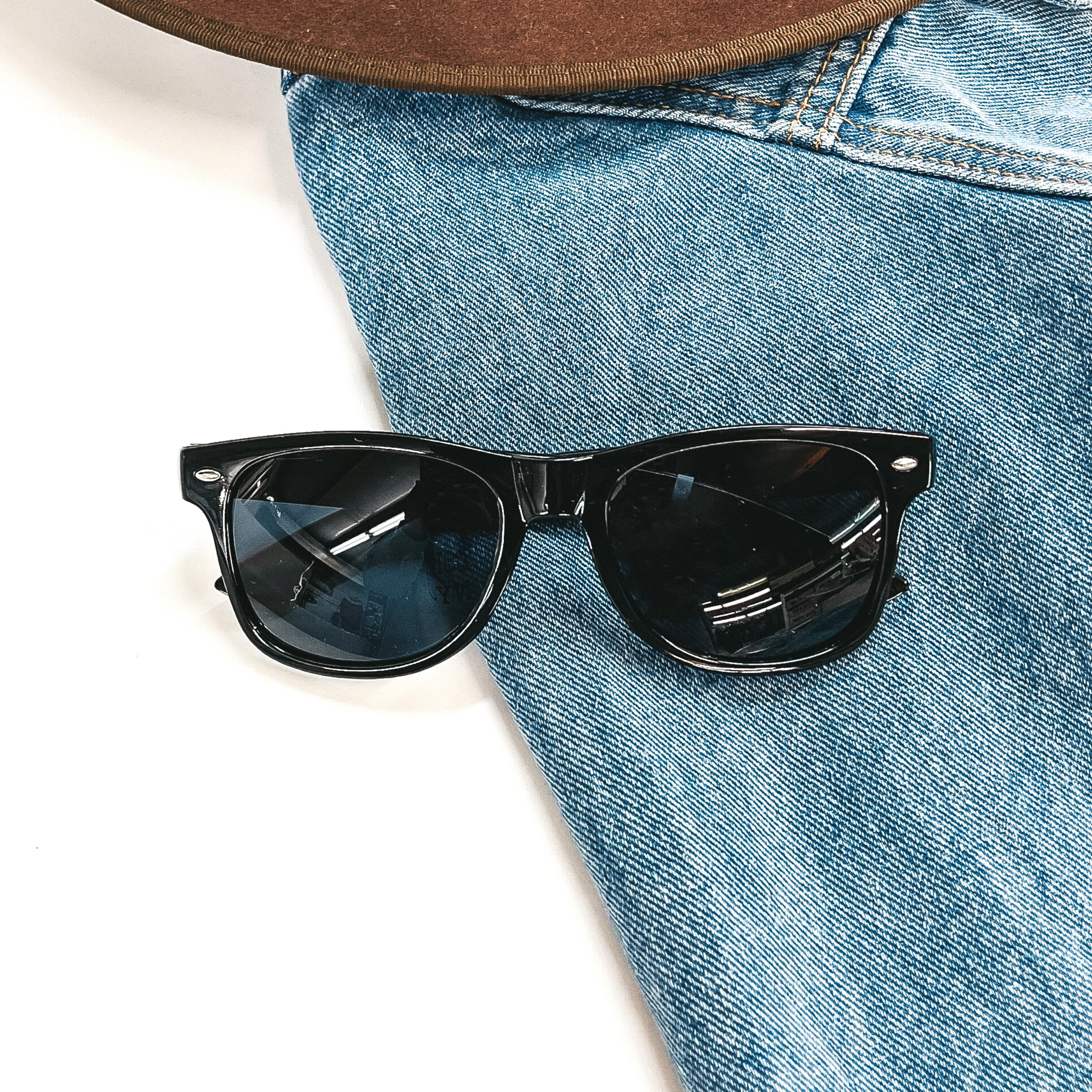 This is a black pair of sunglasses, the lenses are black/dark grey with silver  detailing in the side. These sunglasses are taken on a jean jacket sleeve with a  dark brown felt hat in the top as decor.