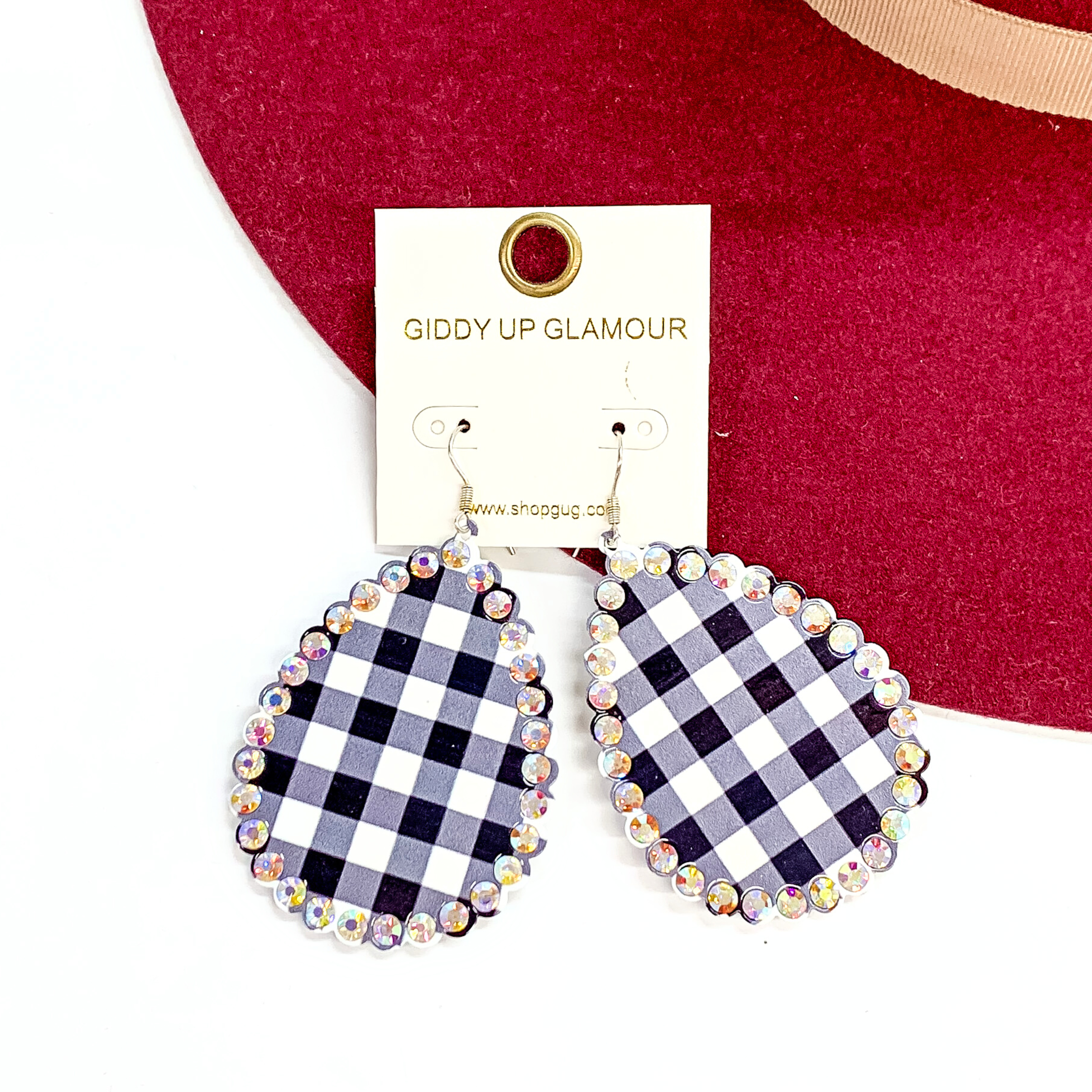 These are teardrop earrings in black and white buffalo plaid print with  scalloped eddges, there are ab crystals all around. These earrings are taken  on a red felt hat brim and on a white background.