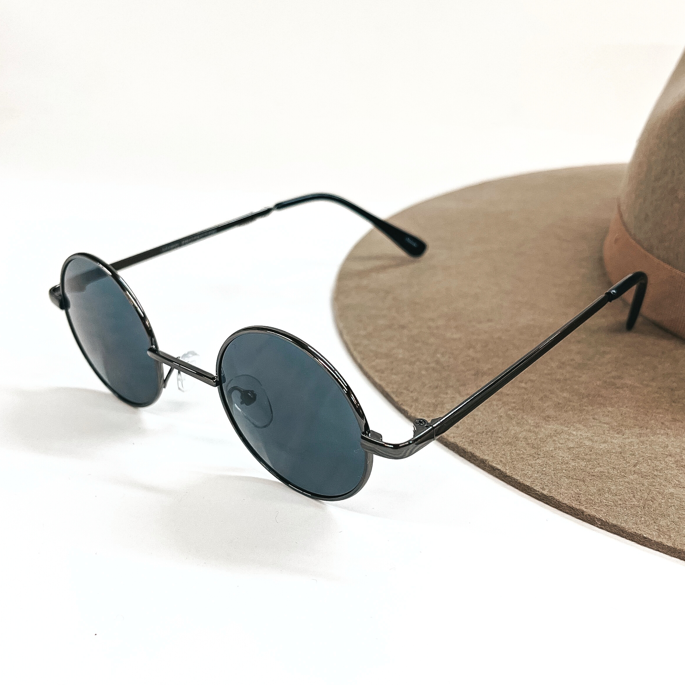 These are small circle sunglasses with black/dark grey lenses and a  gunmetal outline/frame.  These sunglasses are taken on a a white background and on a brown  felt hat brim.