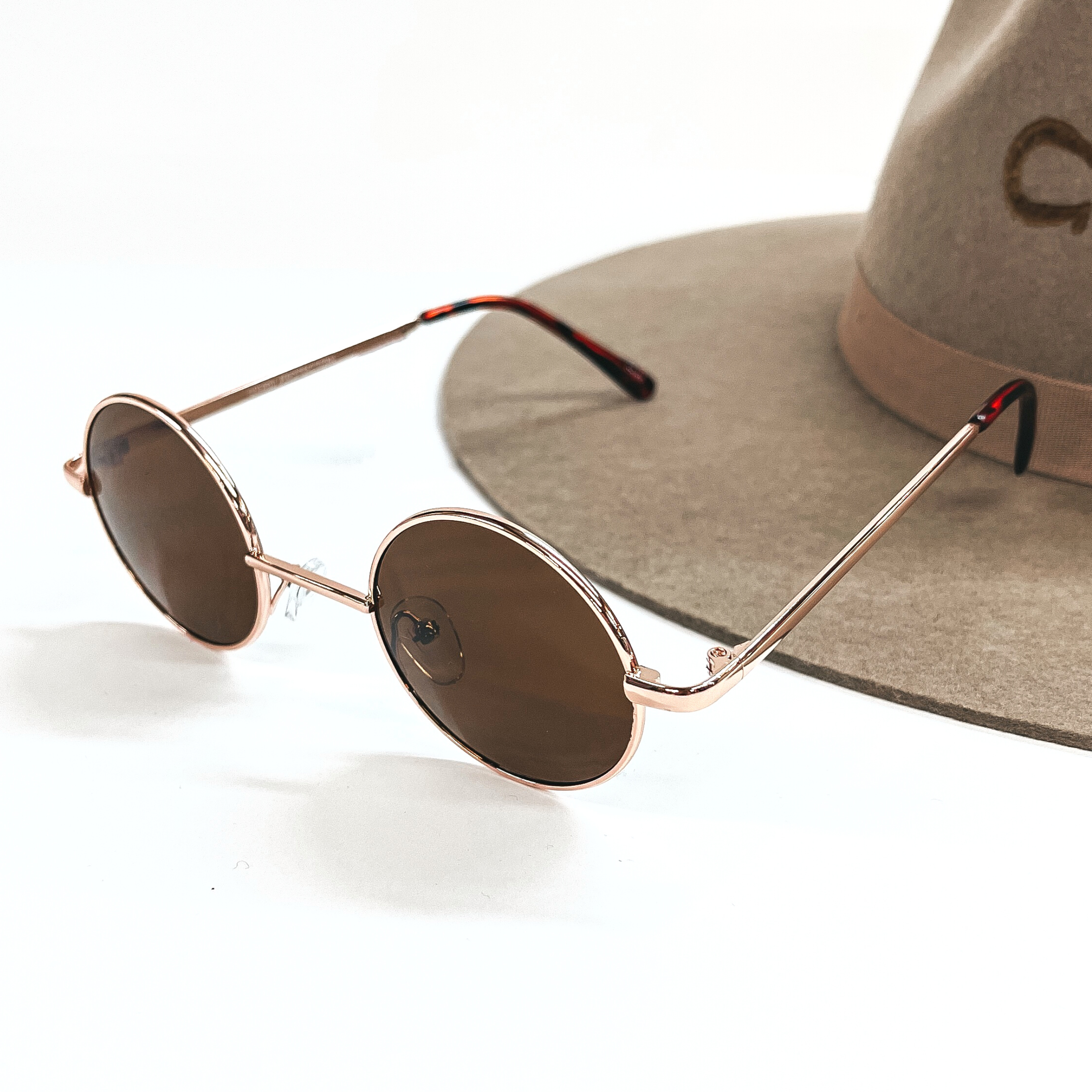 These are small circle sunglasses with brown lenses and a  rose gold outline/frame.  These sunglasses are taken on a a white background and on a brown  felt hat brim.