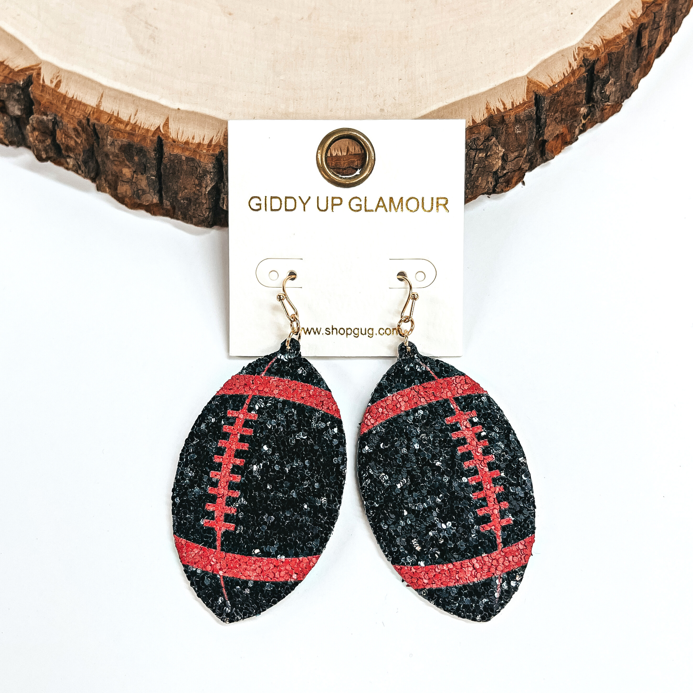 These are football shaped earrings in sequins in red and black. These earrings are leaning up against a slab of wood and on a white background.