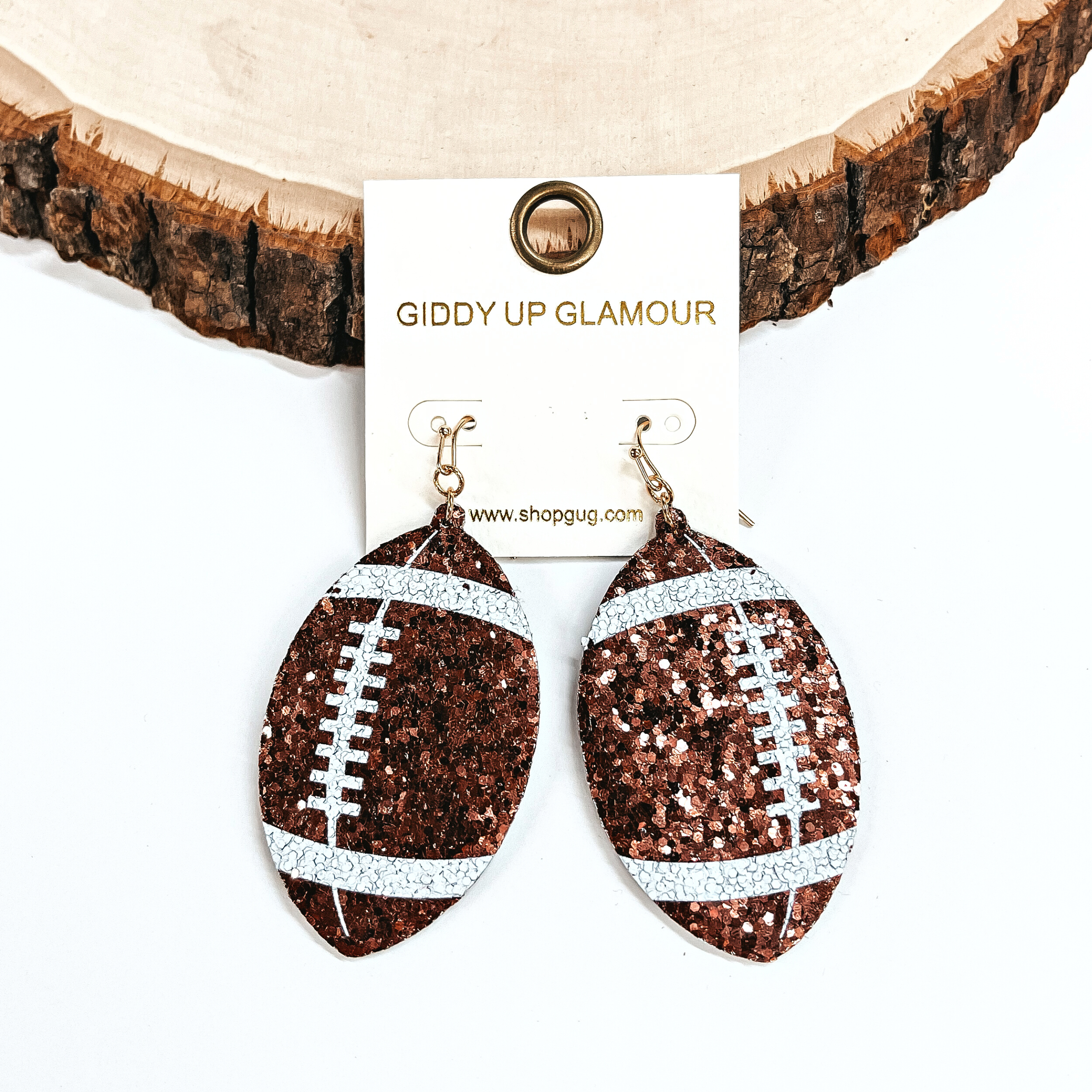 These are football shaped earrings in sequins in brown and white. These earrings are leaning against a slab of wood and on a white background.