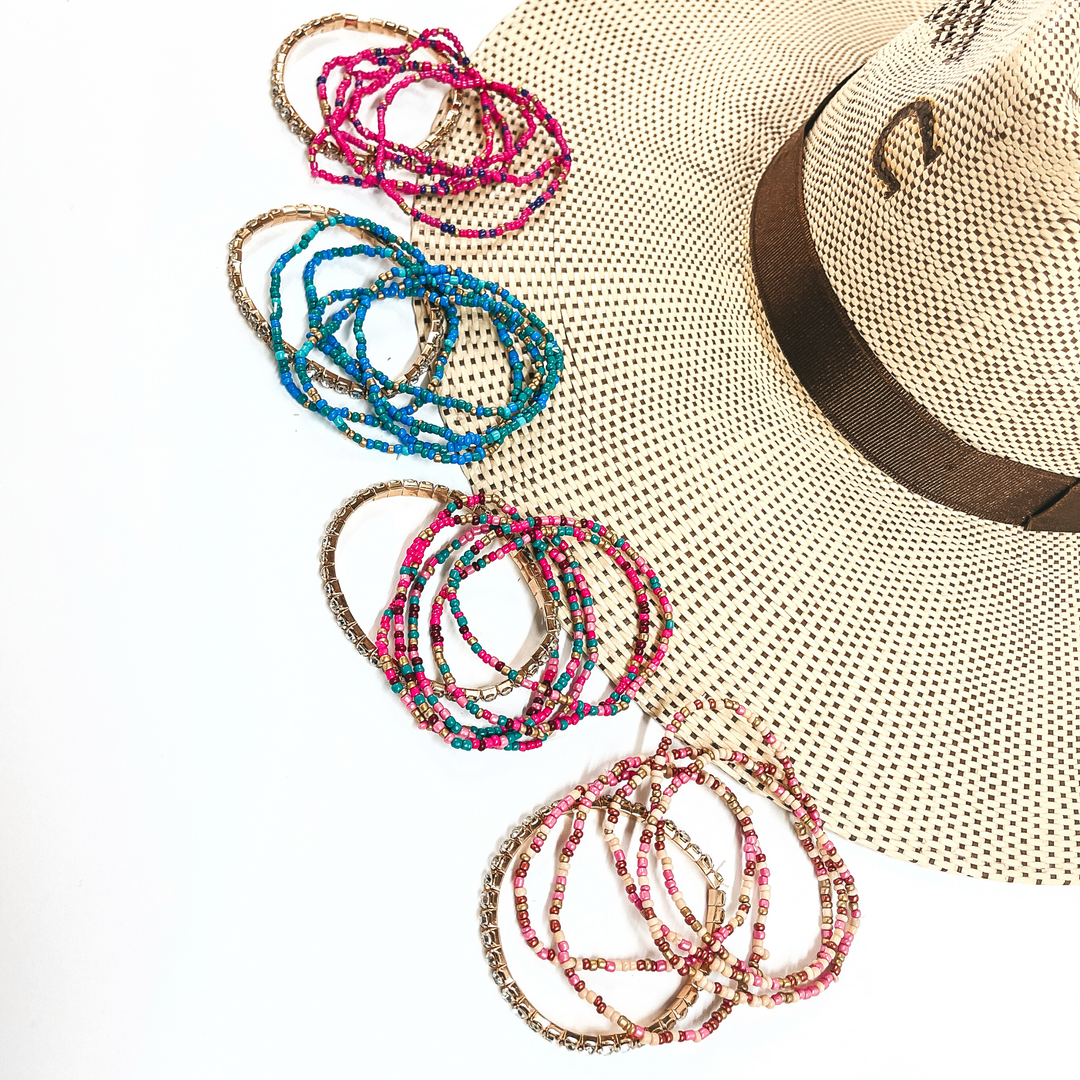There are four sets of six bracelets in different colors in pink/purple mix, blue mix, teal/pink mix, and champagne/pink mix. All bracelet sets have five seedbeaded bracelets in different color combinations and one rhinestone bracelet in a gold setting.