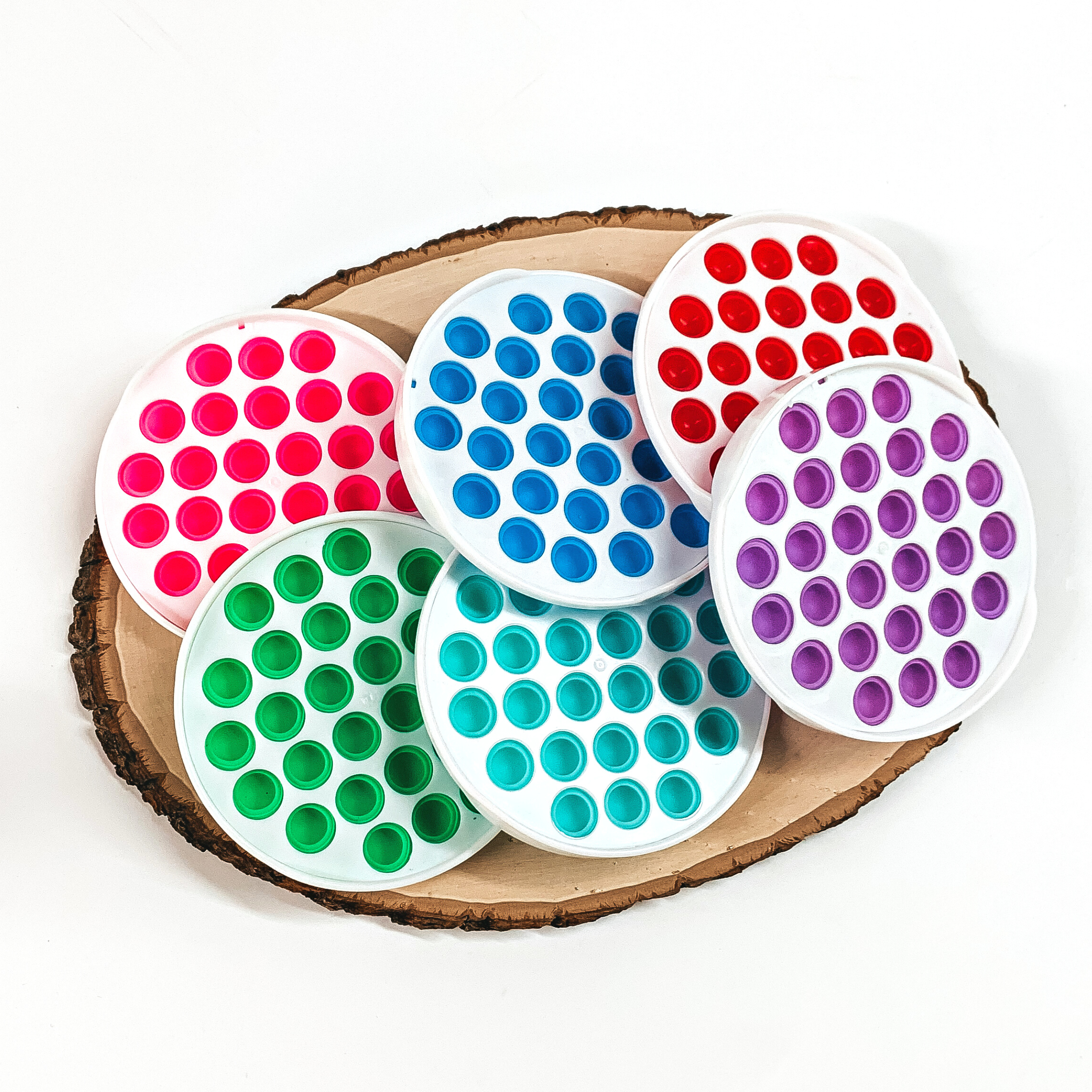 There are six white circle plastic toys with small multicolored circles all around. There is pink, blue, red, green, aqua, and purple. These toys are taken on top of a slab of wood and on a white background.