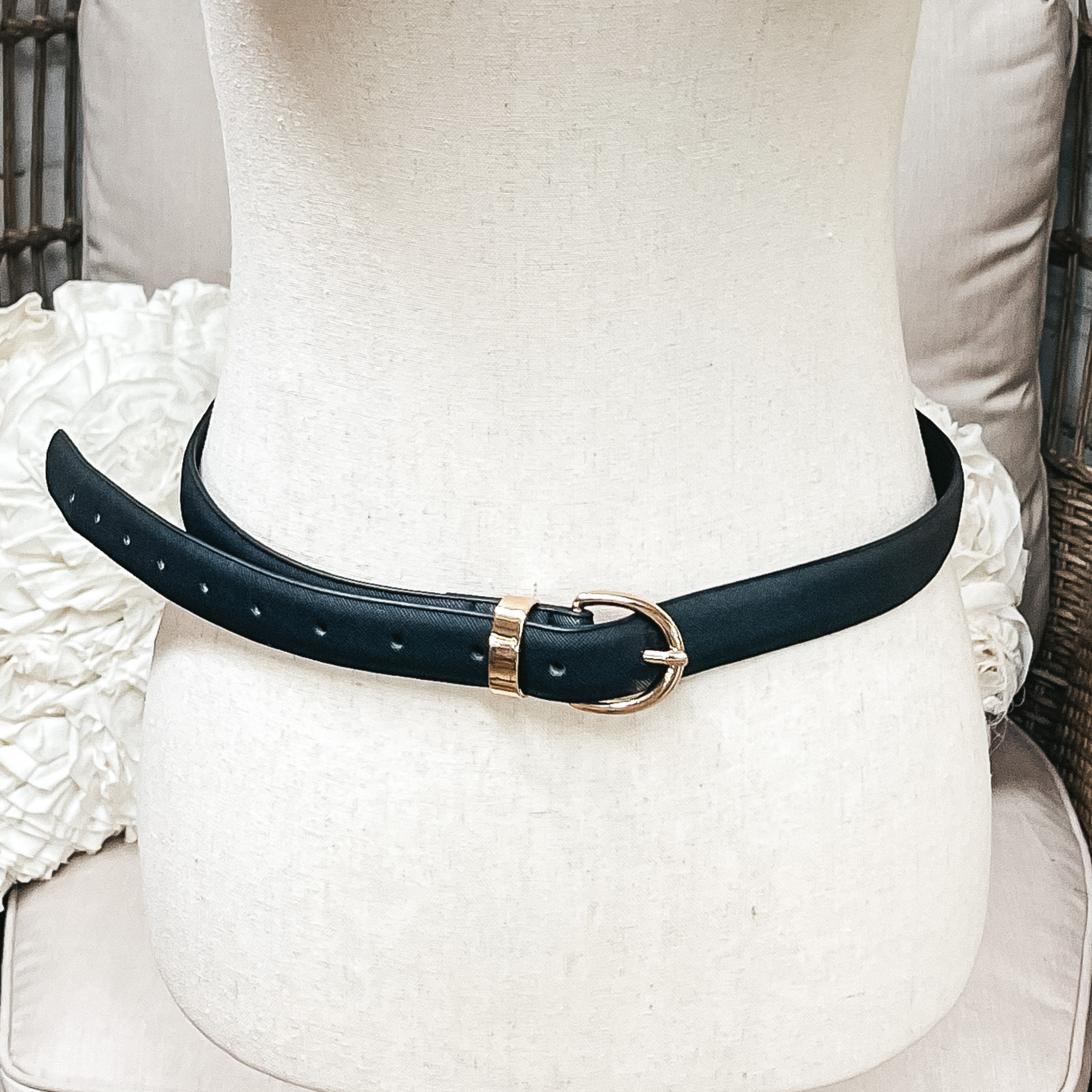 There is one skinny belt in black with a small oval buckle in gold. The belt  is placed on an ivory mannequin.