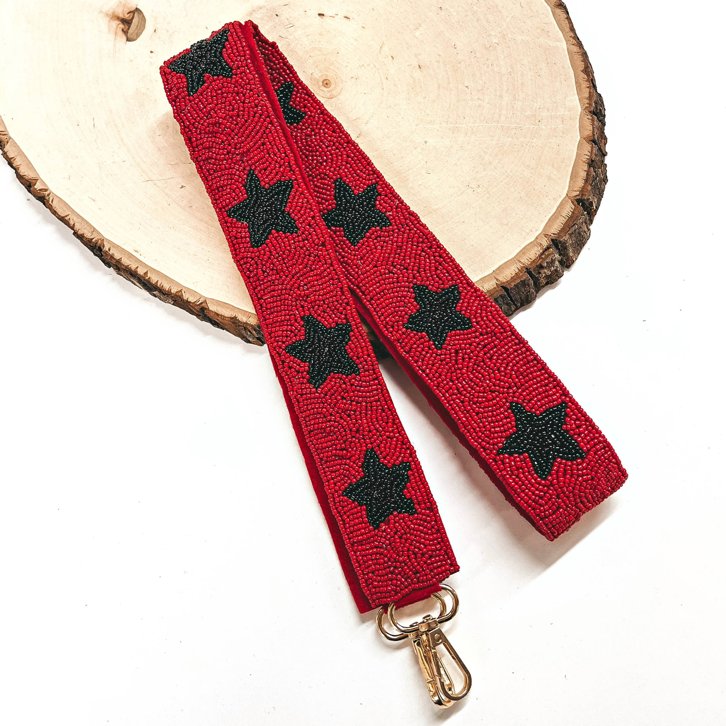 This is a red beaded purse straps with a black beaded stars all along with a gold clasp. This purse strap is taken on a slab of wood and on a white background.