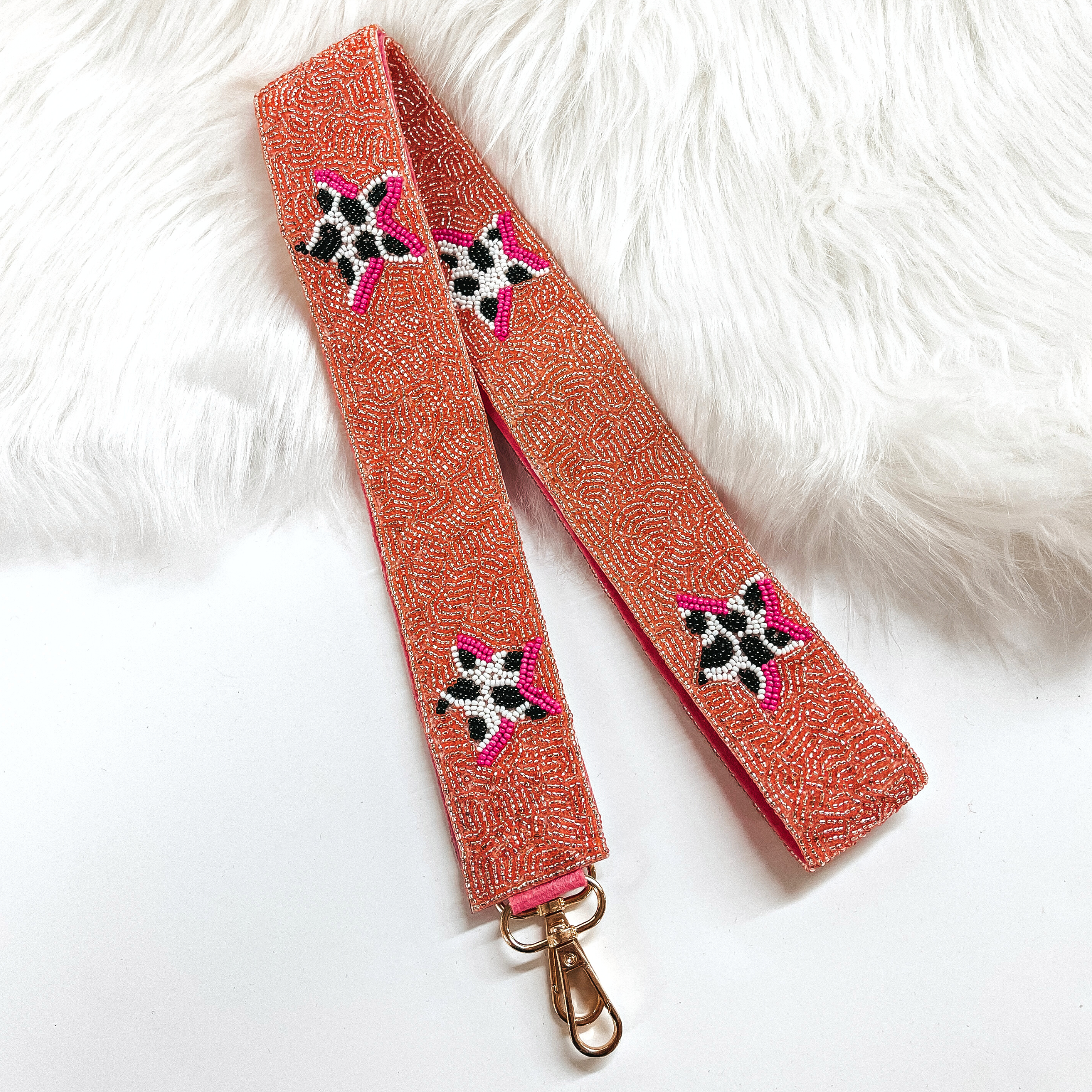 This is a coral pink beaded purse strap with cow print black and white beaded stars all along. This purse strap is laying on a white background and on white fur.