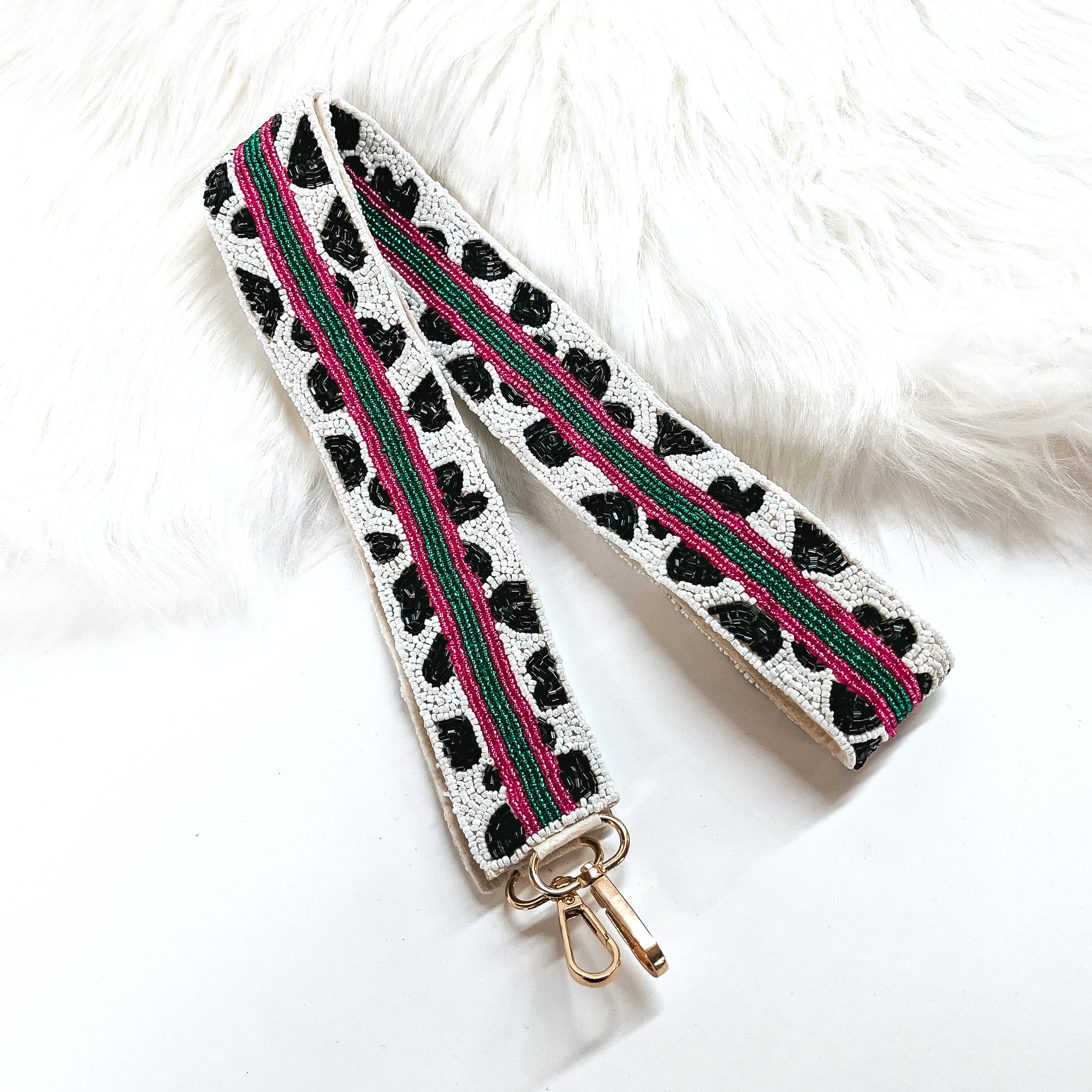 This is a white and black cow print beaded purse strap with three strap all along in pink and green, with gold clasps. This purse strap is taken on a white background and on white fur.