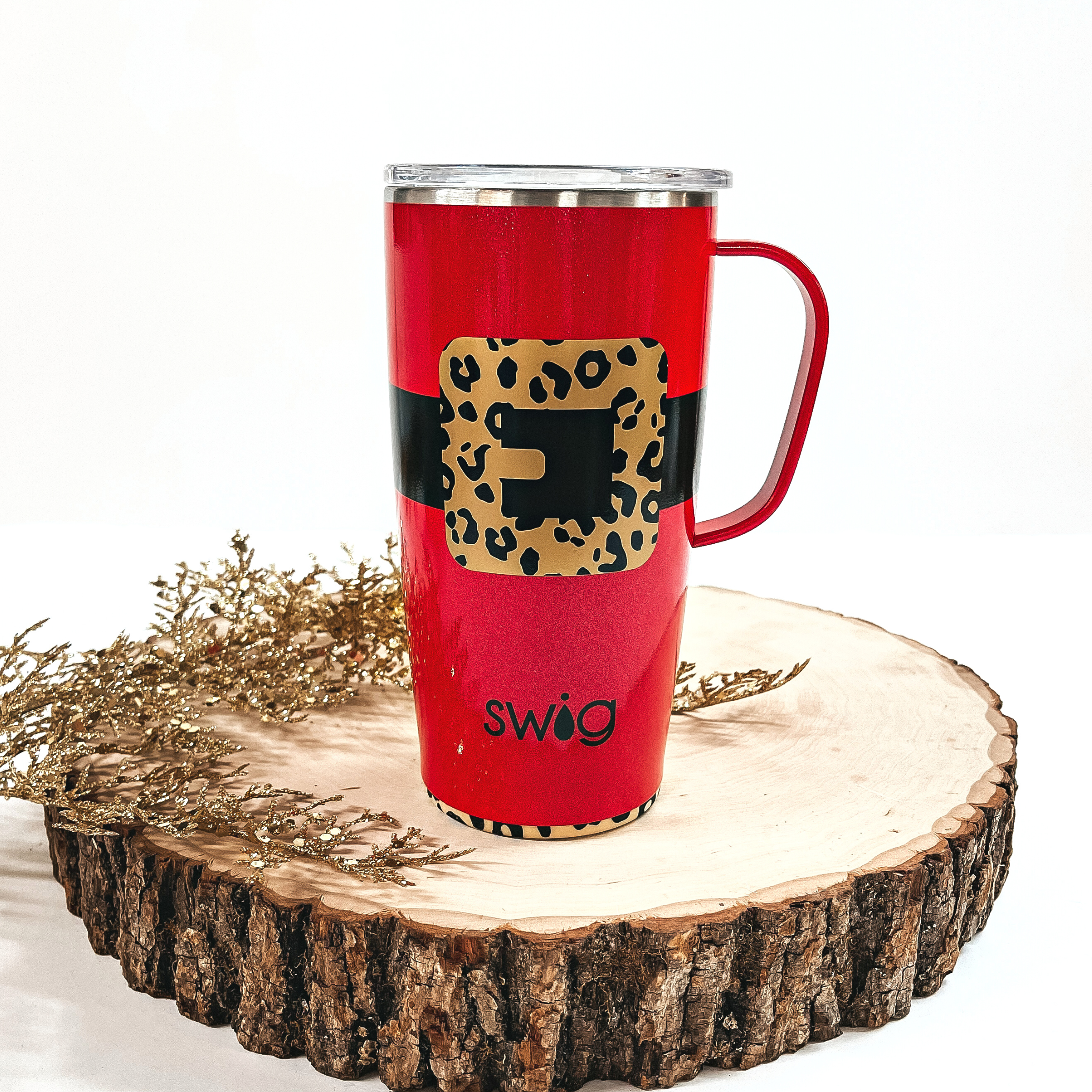 This is a red cup with a black thick line all around and a gold/black  leopard print buckle. It has a red handle, top and a leopard print bottom. This cup is taken on top of a slab of wood and on a white background, with  a gold sparkly plant in the side as decor.