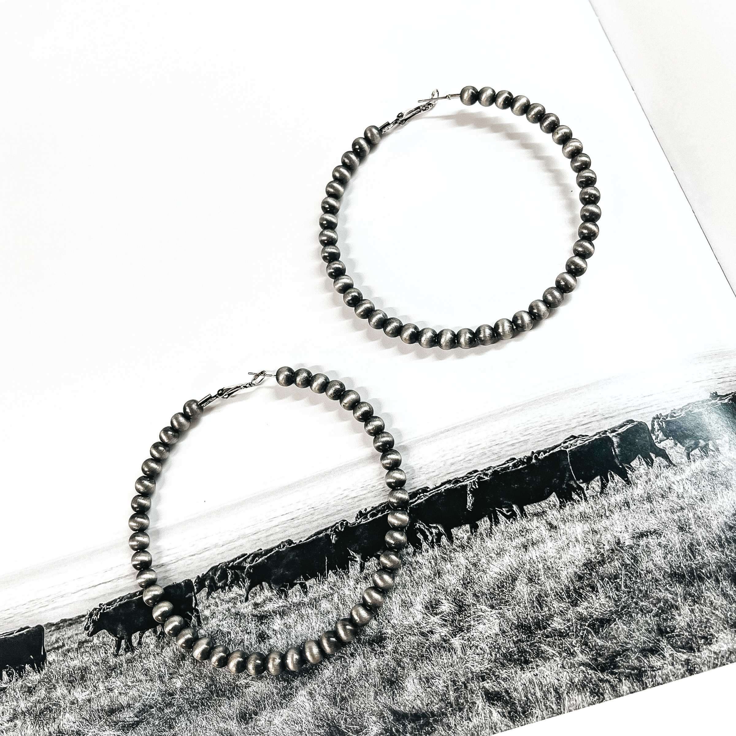 These are large silver beaded hoop earrings. These earrings are taken on a black and white outdoor page.