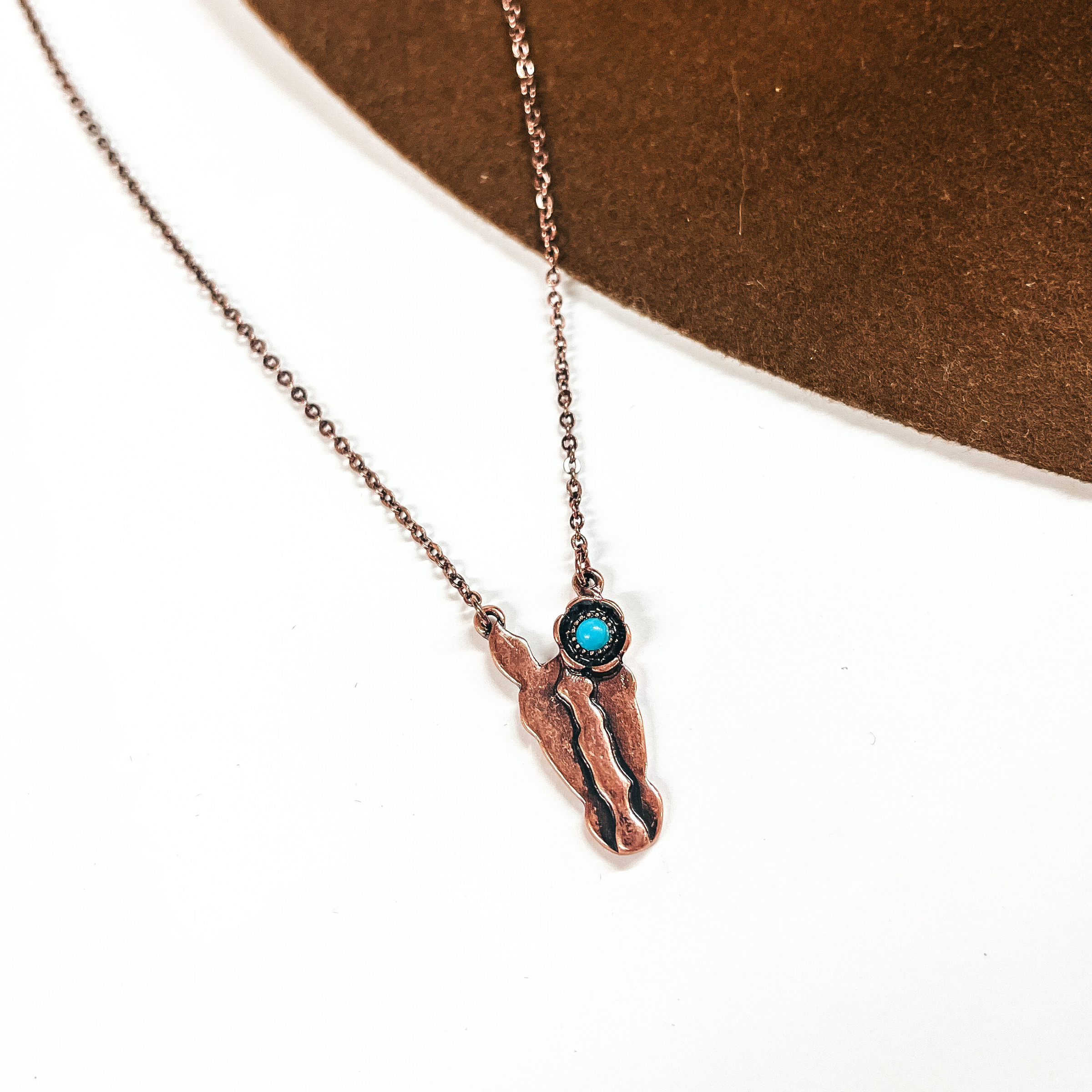 This is a copper chain necklace with a horse head pendant, has a small turquoise stone on one ear. This necklace is taken on a white background and on a dakr brown felt hat brim.