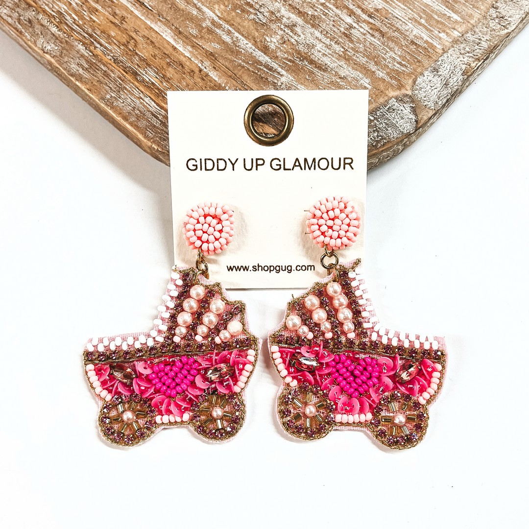 These are pink beaded stroller earrings with pearls, rhinestones, and sequins. These earrings are taken on a white background and leaning up against a light wood of slab. 