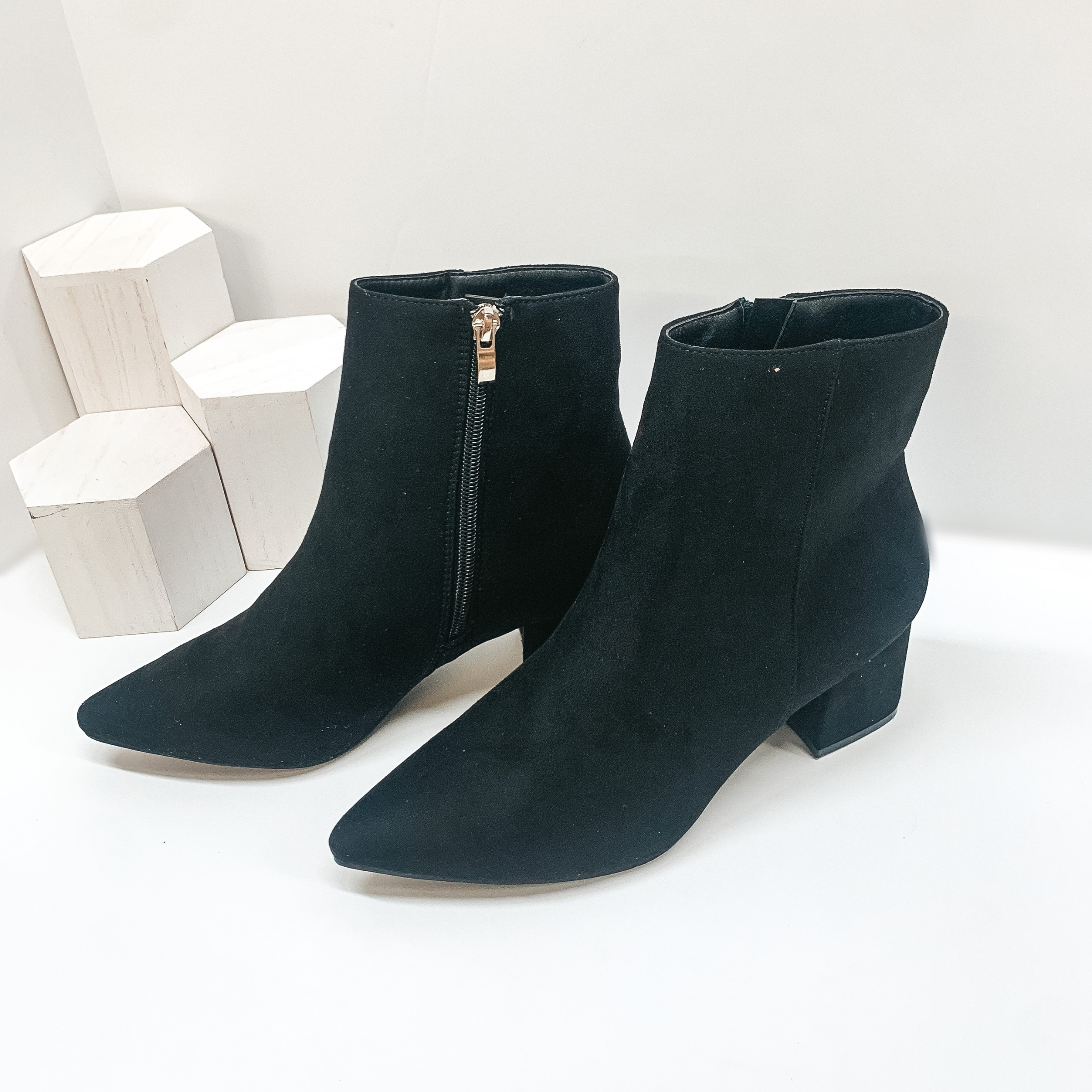Suede Pointed toe block heel ankle booties with inside ankle zipper closure in black. These booties are pictured on a white background with white blocks in the background. 