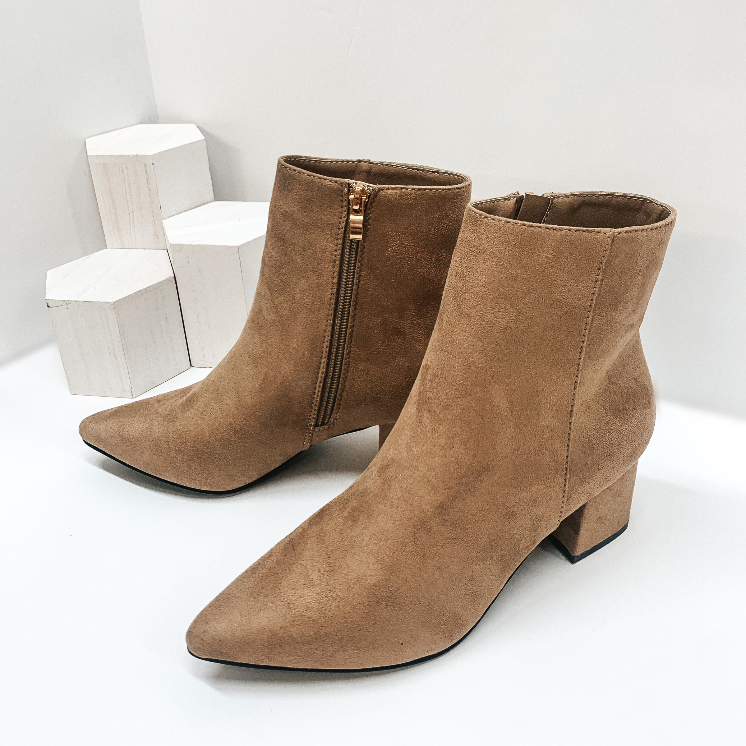 Suede Pointed toe block heel ankle booties with inside ankle zipper closure in taupe. These booties are pictured on a white background with white blocks in the background.