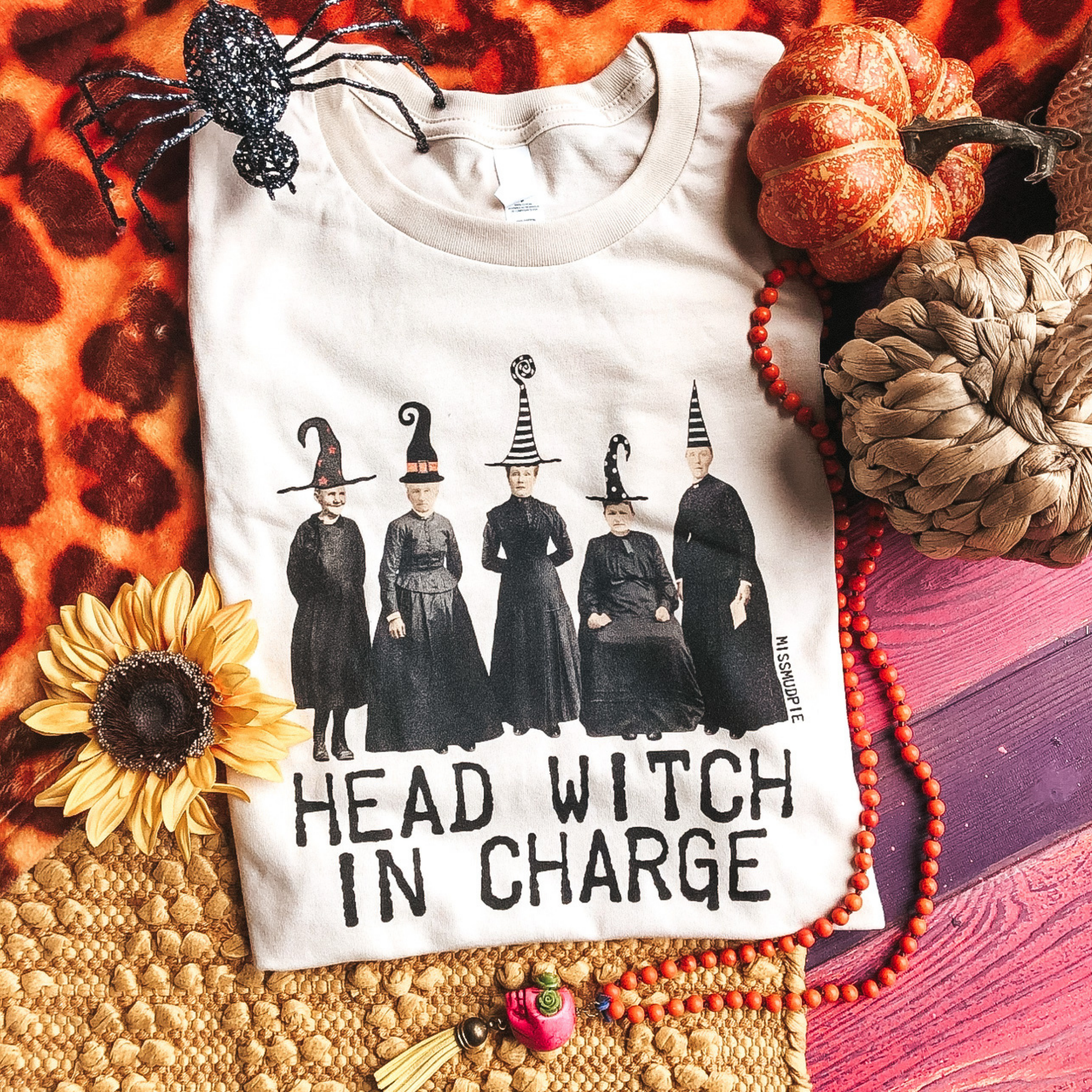 Cream tee shirt with 5 witches lined up with words "head witch in charge" below.  Shirt seen with pumpkins, sunflower, spider and cute decorations.
