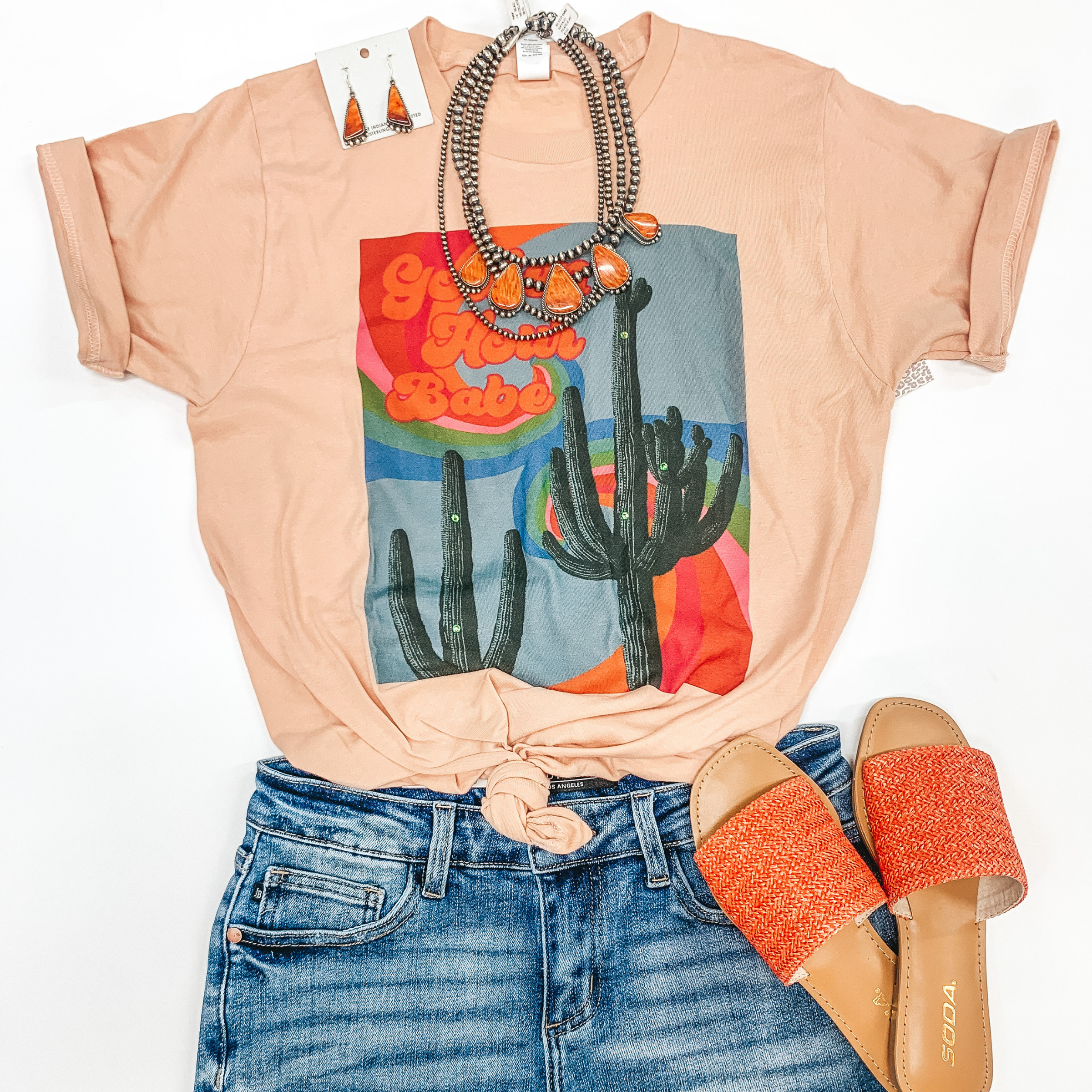 Peach pink tee with a rectangular print depicting two cactuses with a colorful wave behind it and the words  "golden hour babe" written in a retro font overtop. 