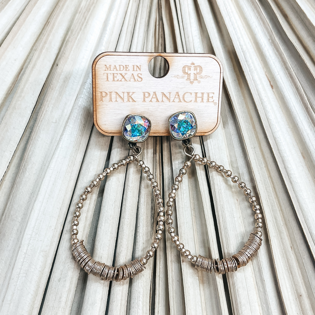 Post back teardrop earrings with an AB cushion cut  crystal. The teardrop has matte gold circle beads with small square beads. In the middle there are gold metal disk beads. Taken on a dried up palm leaf.