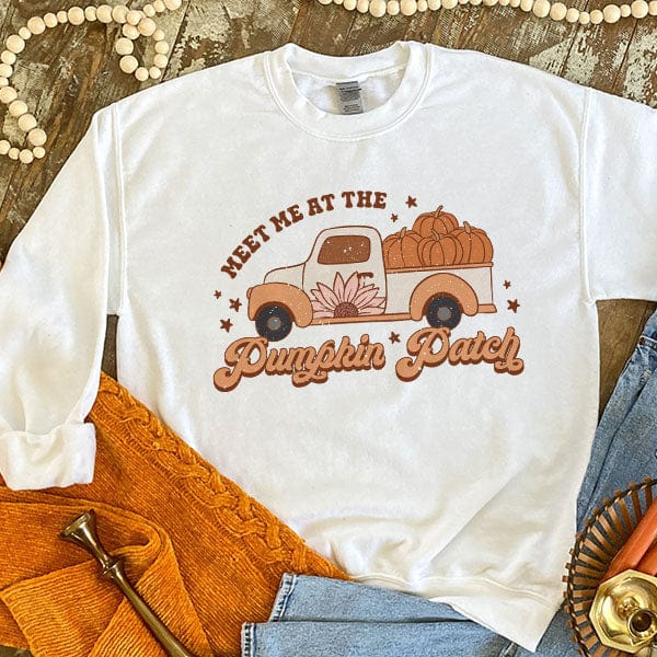 This white sweatshirt includes a crew neckline, long sleeves, and a hand drawn graphic with words "Meet Me At The Pumpkin Patch" around a Fall truck with pumpkins in the back. This is a Bella + Canvas Tee and styled in this photo as a flat lay with rolled sleeves and paired with a light wash denim pair of jeans.