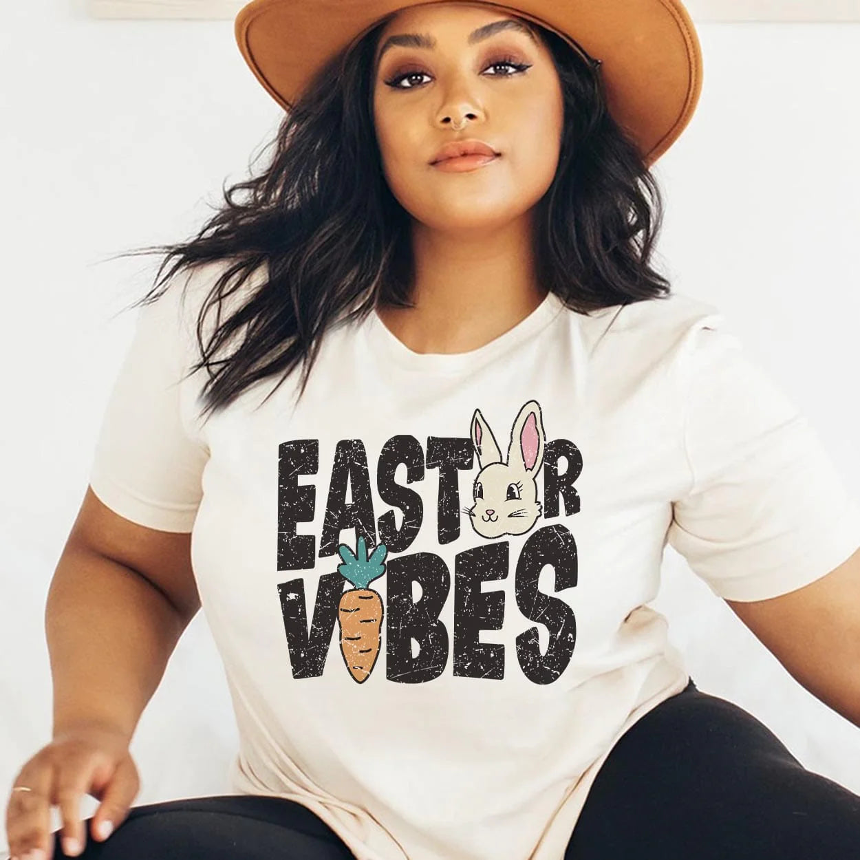A cream colored short sleeve tee with the words "Easter Vibes" in the center with a bunny for the second E in Easter and a carrot for the I in vibes, Item is pictured on a white background.
