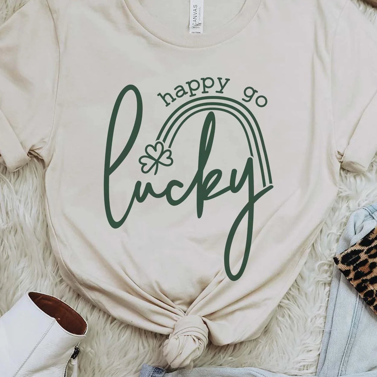 A cream crew neck sweatshirt featuring the words "Happy go lucky". "Lucky" being in the center in cursive while "happy go" is above "lucky" in a smaller font. Between the two is a small rainbow with a clover at the end. Item is pictured on a white background.