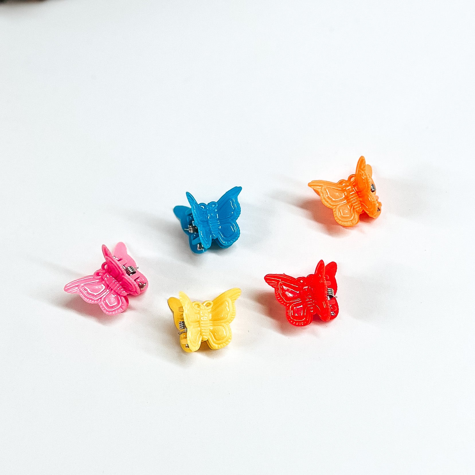 Small, solid color butterfly hair clips. There are five clips pictured on a white background in colors pink, yellow, blue, yellow, red, and orange. 