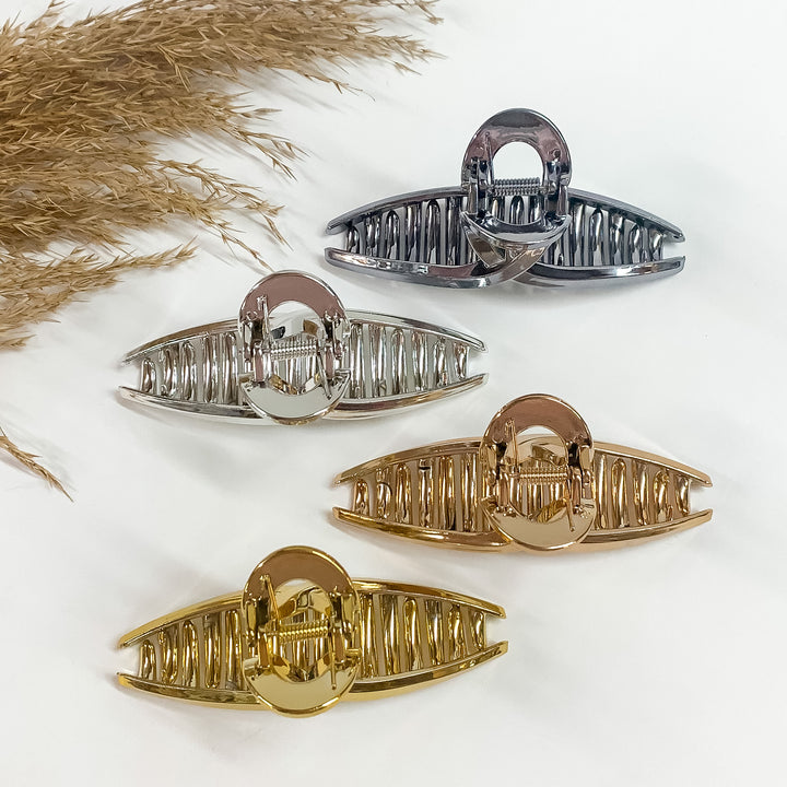 There are four loop clips in metallic laying on a white backround  with a brown plant in the side as decor. There is gunmetal, silver, copper,  and gold.