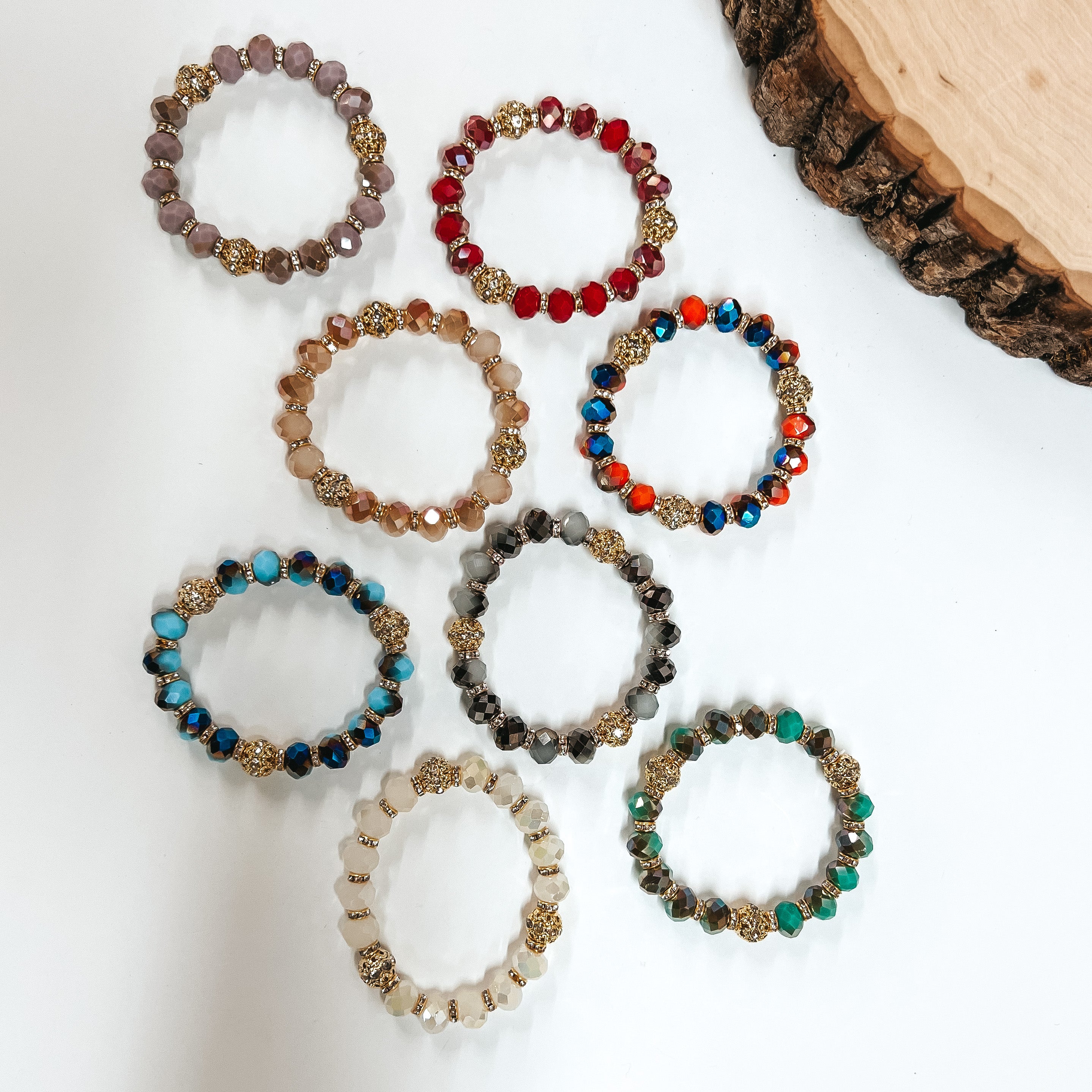 There are eight crystal beaded bracelets placed on a white background with a slab in the corner as decor. There are different color combinations and textures.