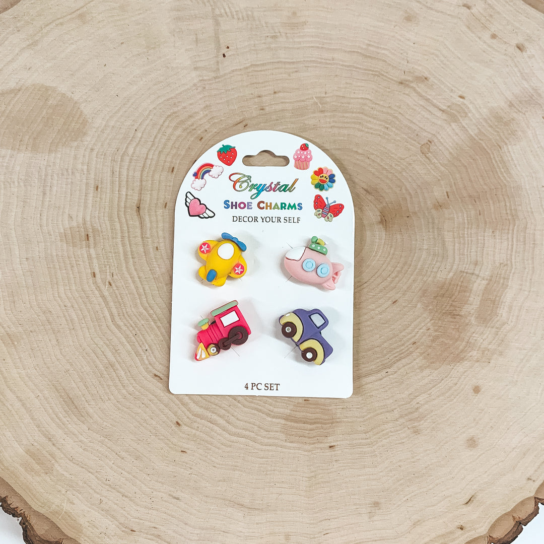 This is a pack of four small shoe charms in different colors and figures such as a plane, train, truck, and a submarine. These shoe charms are placed on a white card and taken on a slab of wood.