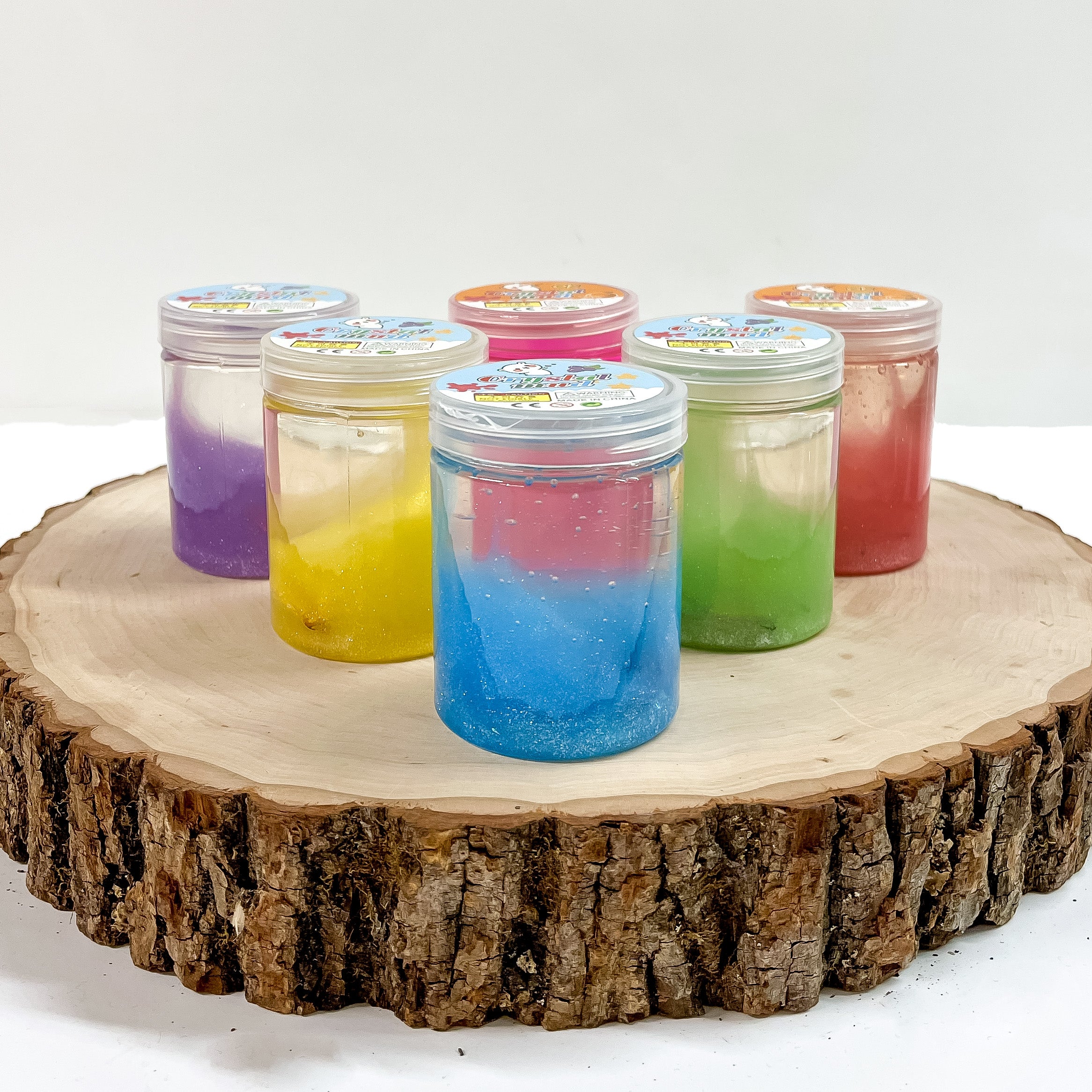 There are six small clear containers with different colors in a traingle shaped. These clear slimes are taken on a slab of wood and on a white background.
