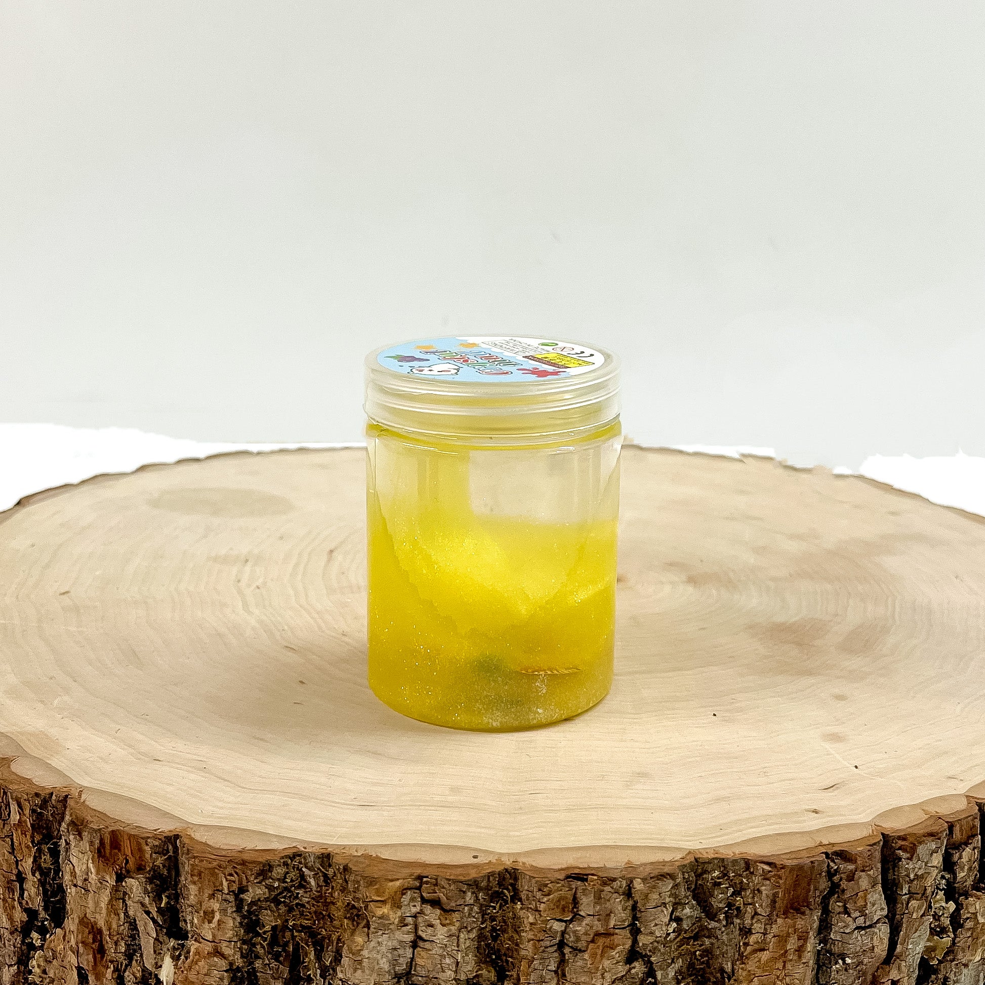 This is a clear slime with yellow glitter, this container is taken on a slab of  wood and on a white background.