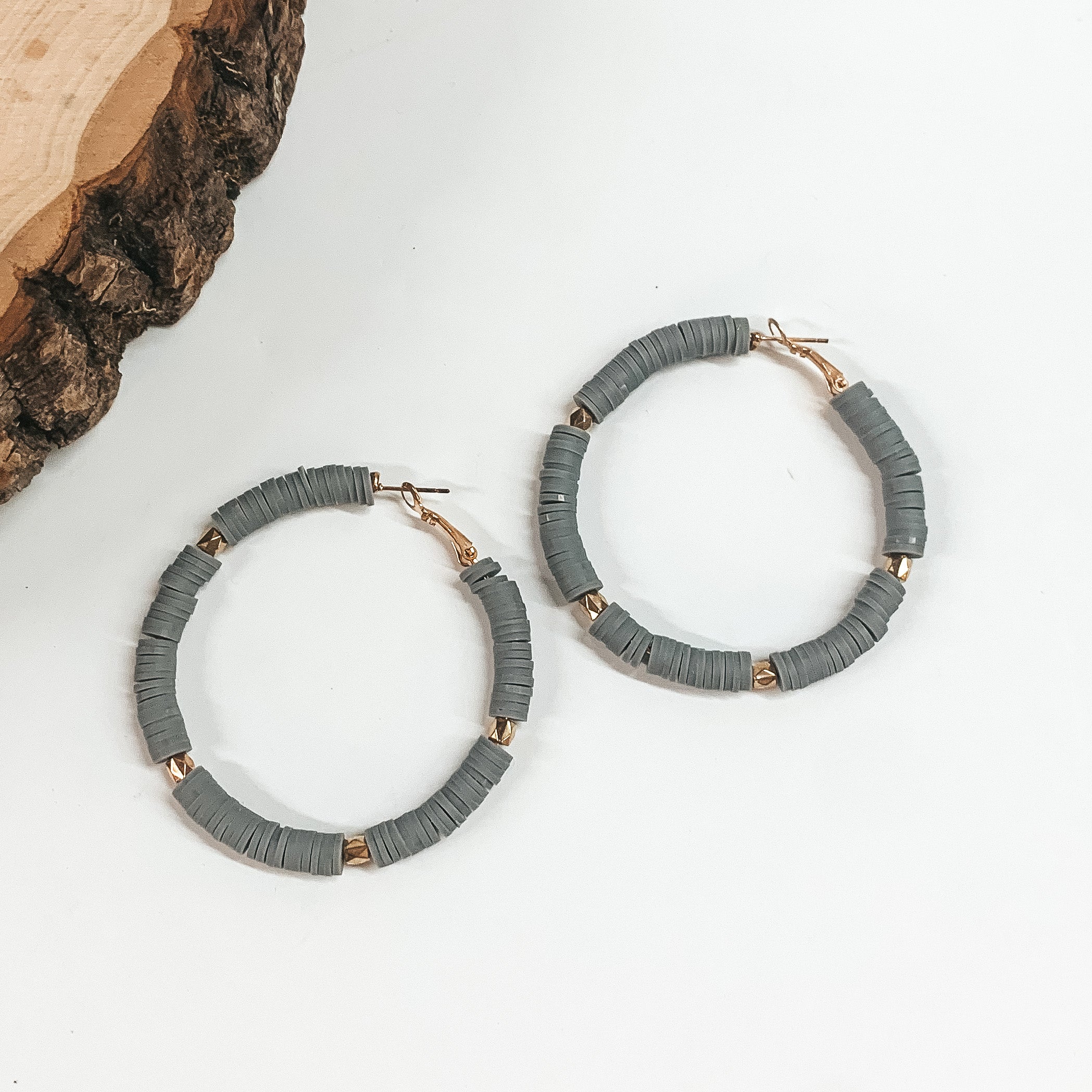 This is a pair of gray disc beaded hoop earrings with gold spacers. These  earrings are taken on a white background with a slab of wood in the back  as decor.