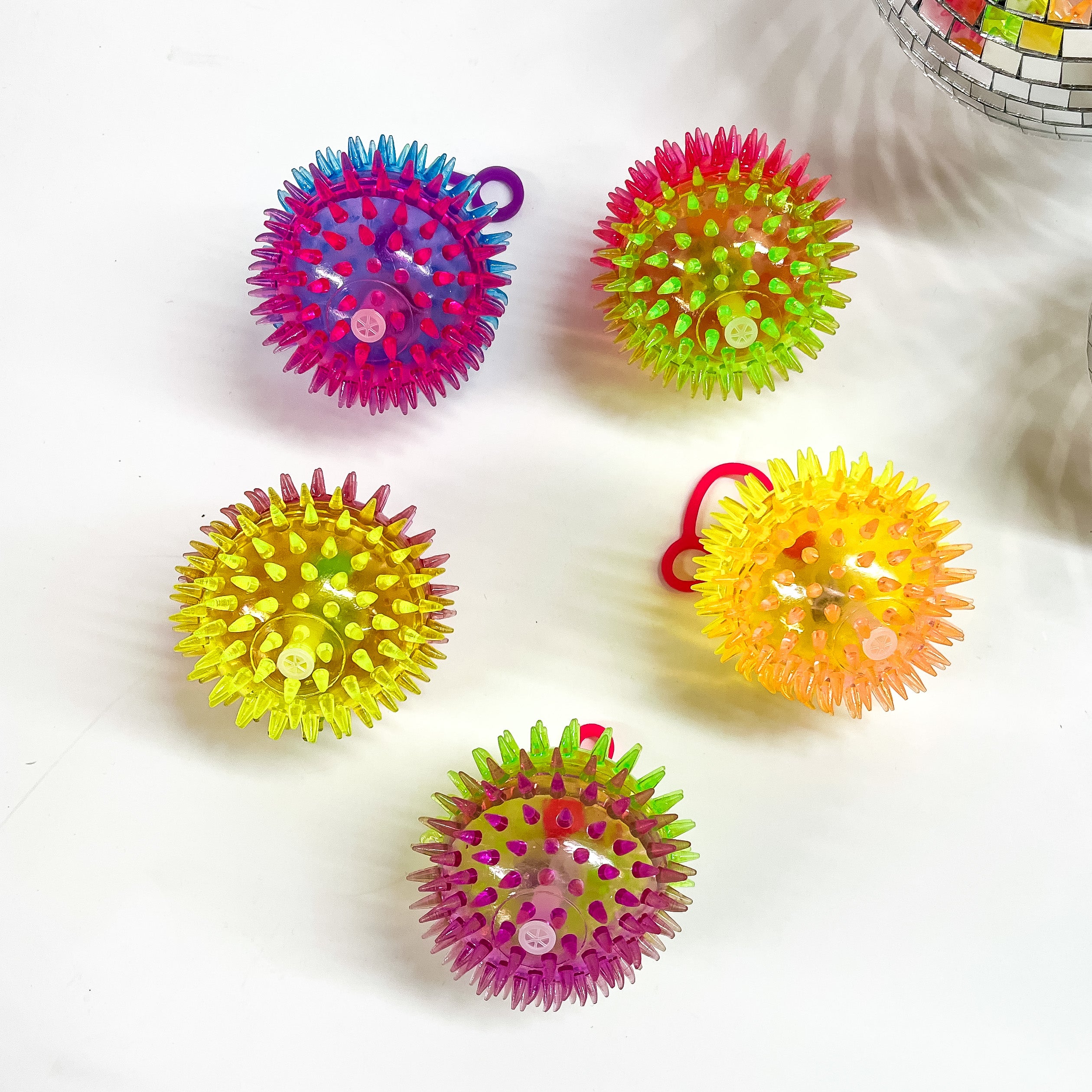 There are five spike balls with different color combinations, all spike balls comes with a stretchy finger holder and all spike balls have a ligt inside. These spike balls are taken on a white background with a disco ball in the corner as decor.