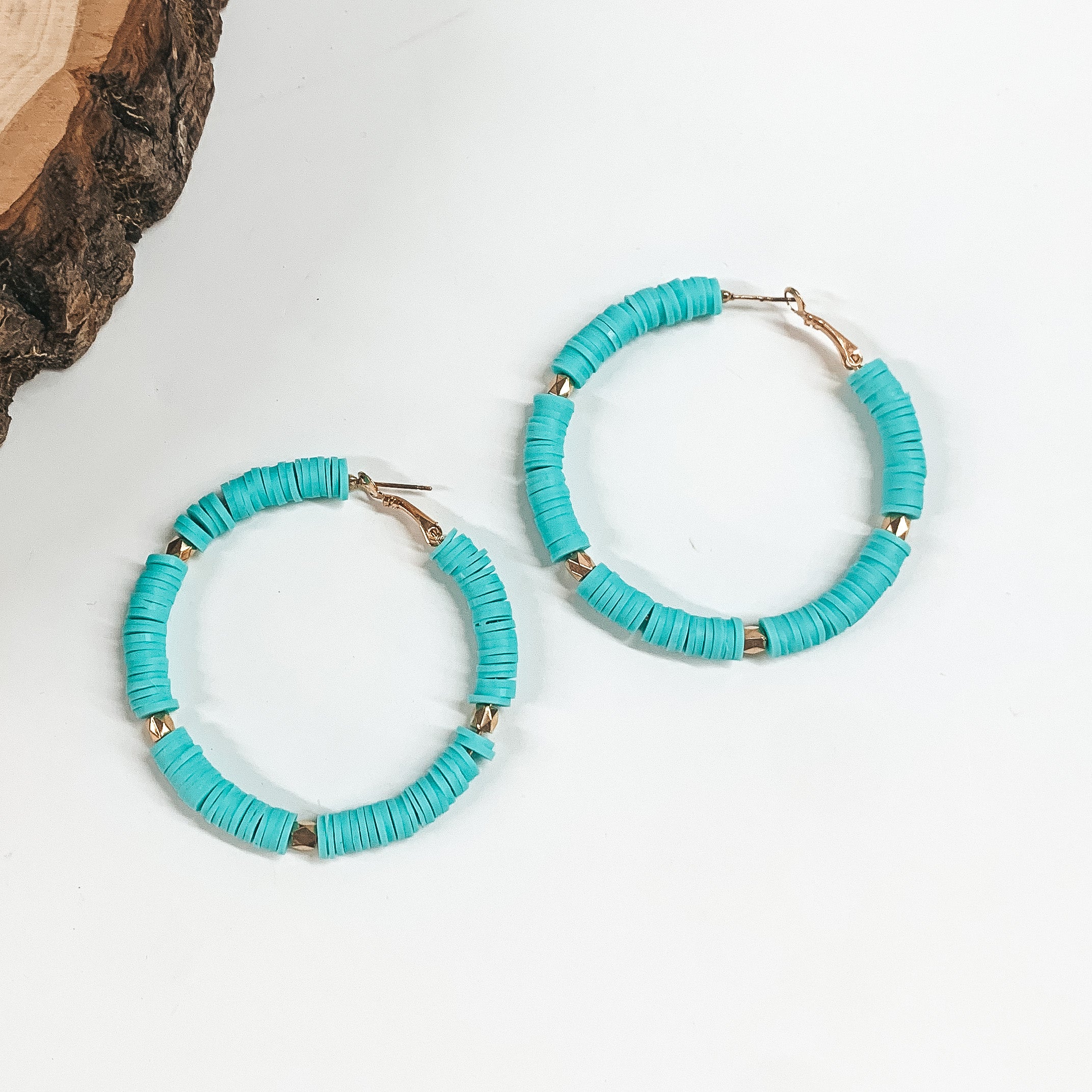This is a pair of turquoise disc beaded hoop earrings with gold spacers. These  earrings are taken on a white background with a slab of wood in the back  as decor.