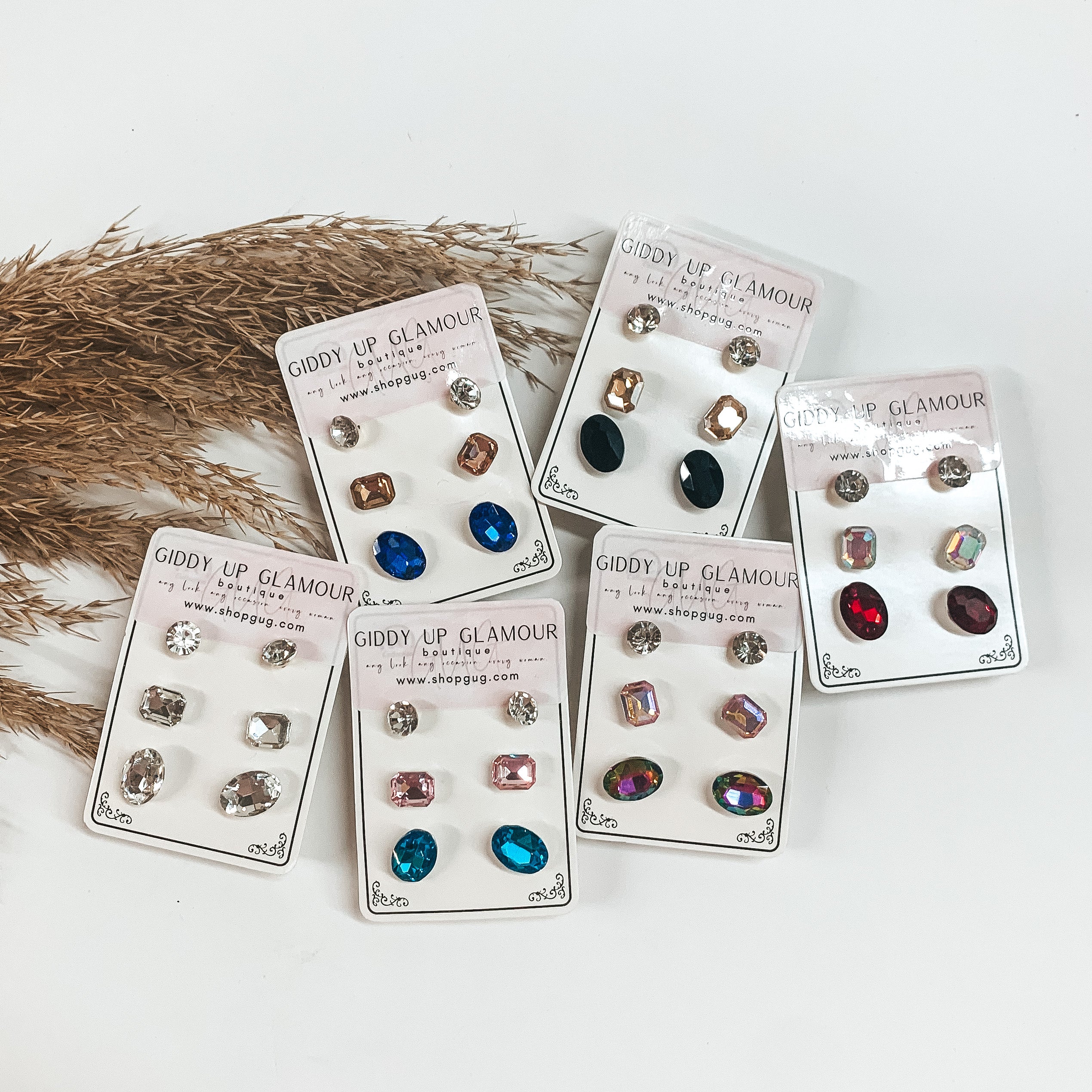 Pictured are six sets of earring sets. These earrings are pictured on a white background with tan pompous grass. 
