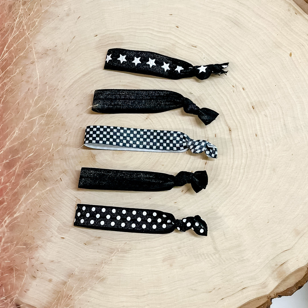 Siz black hair ties pictured on a wood block. 2 hairties are solid black and the rest have a white design. 