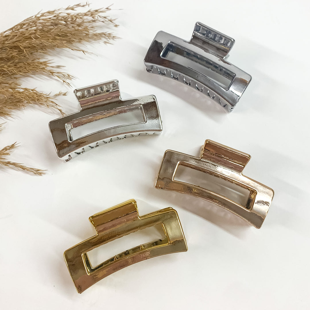 There are four rectangle clips in metallic laying on a white backround  with a brown plant in the side as decor. There is gunmetal, silver, copper,  and gold.