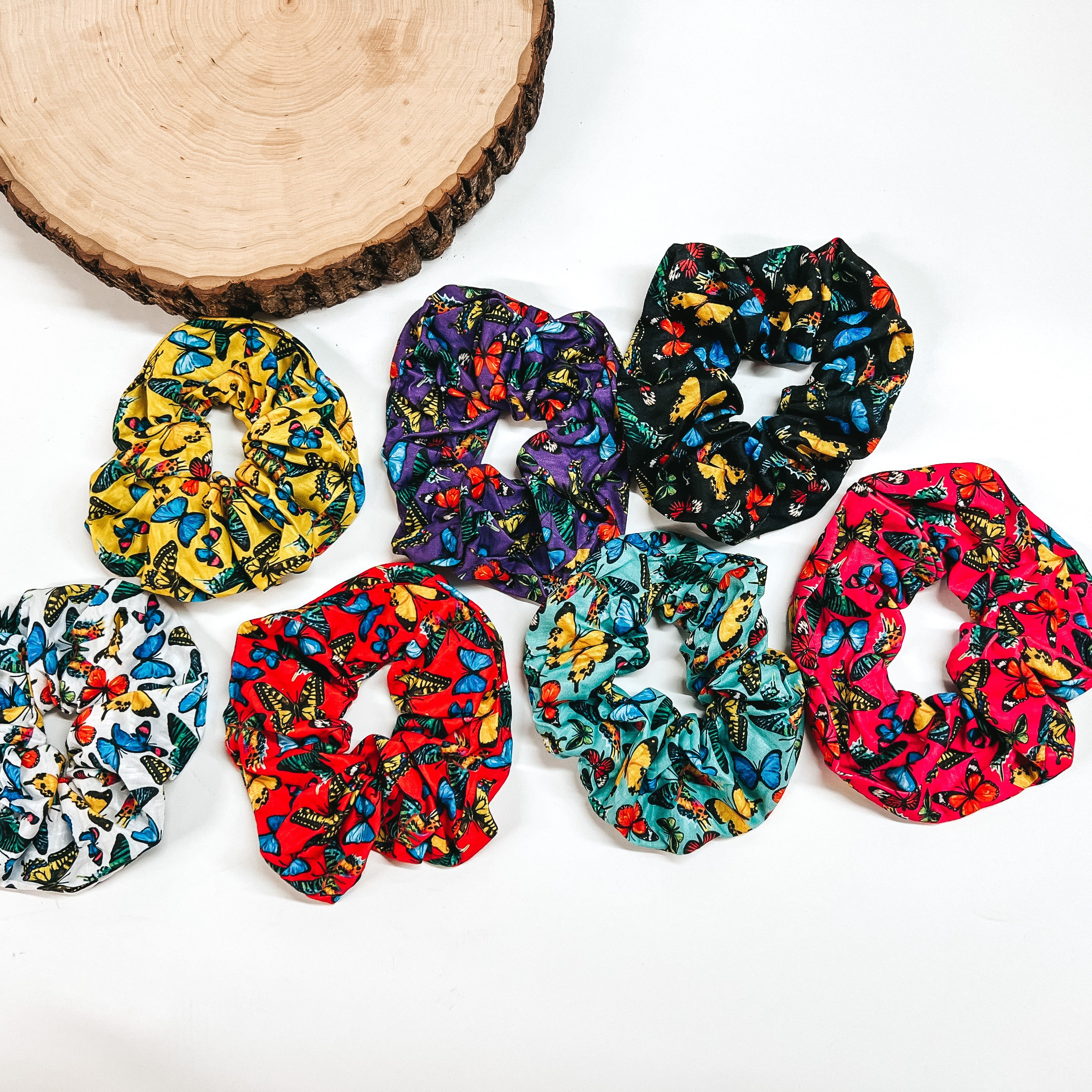 Seven different colored scrunchies with the same butterfly design is pictured on a white background. 