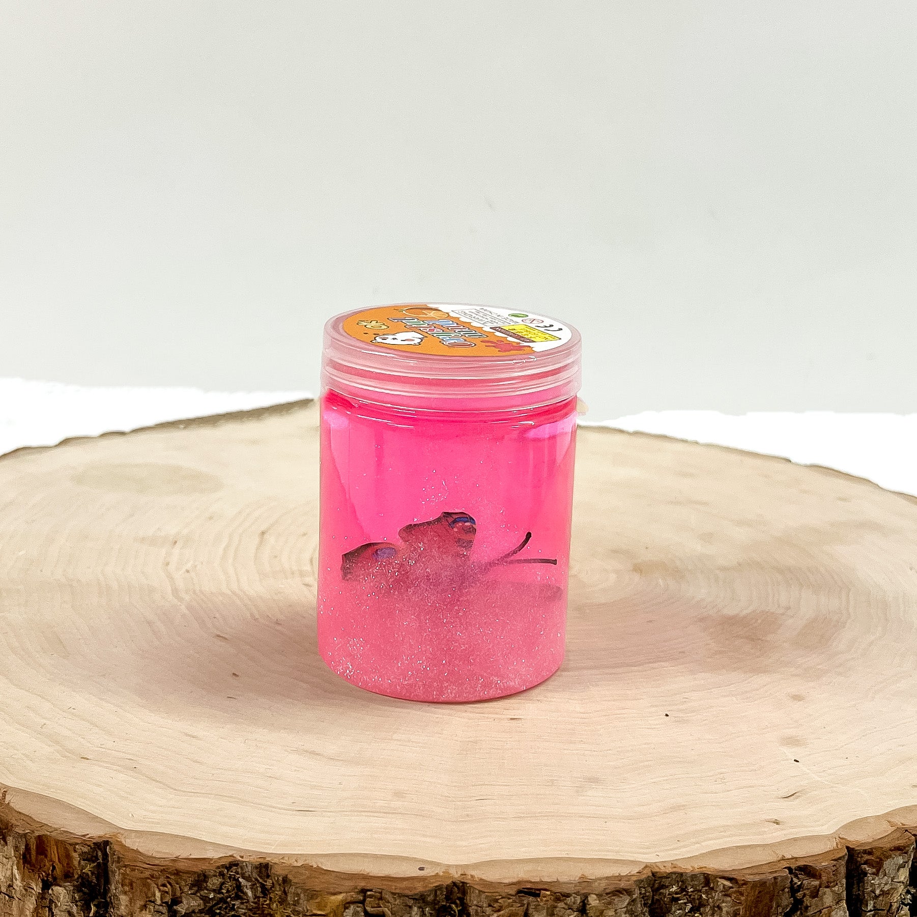 This is a clear slime with pink glitter and a butterfly, this container is taken on a slab of  wood and on a white background.