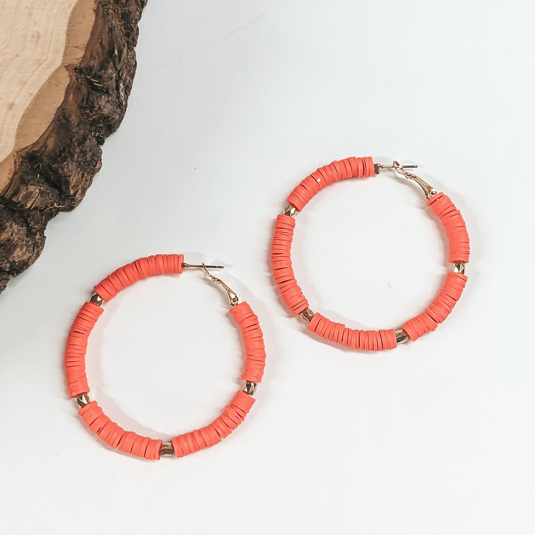 This is a pair of coral disc beaded hoop earrings with gold spacers. These  earrings are taken on a white background with a slab of wood in the back  as decor.
