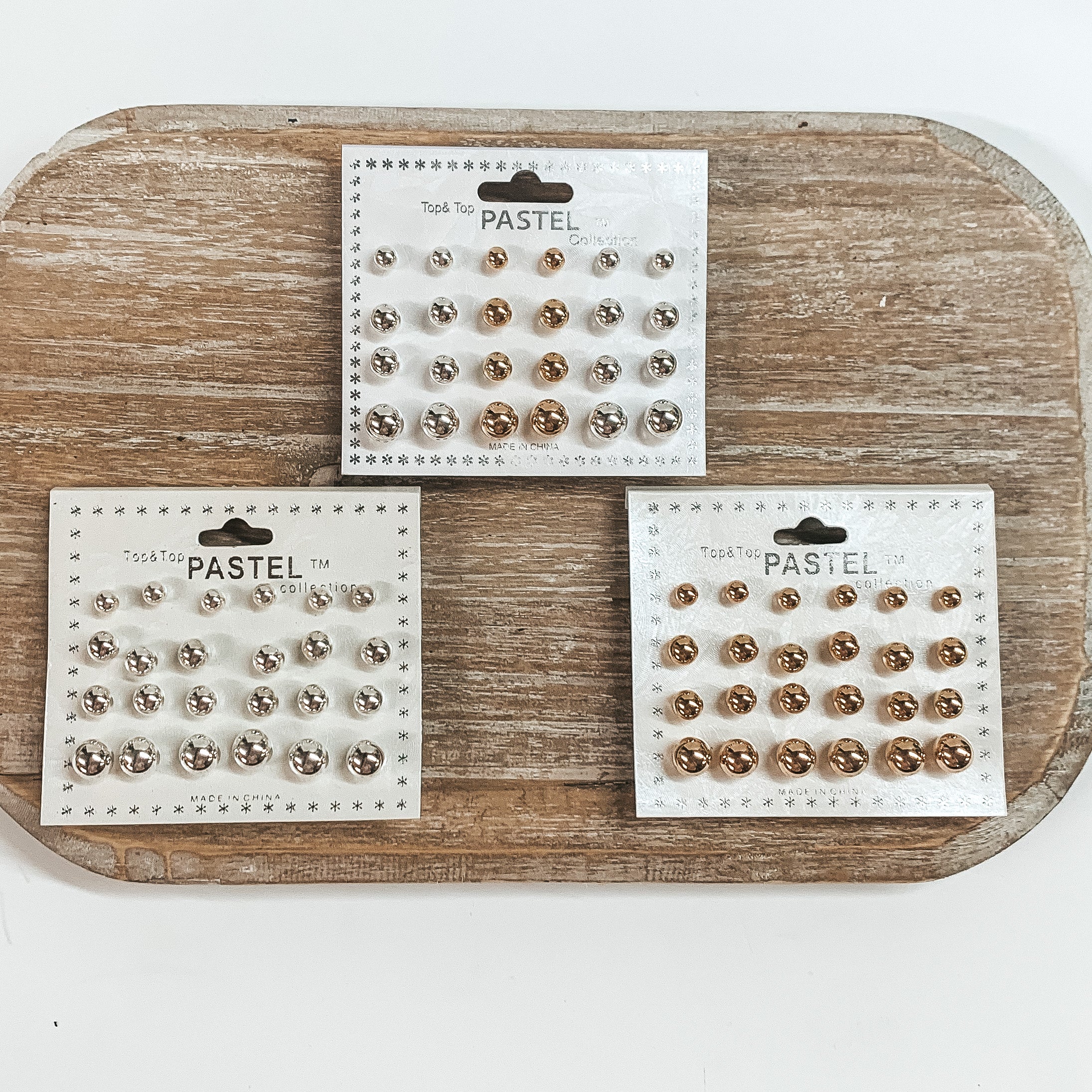 There are three packs of twelve stud earrings on a white earring card holder. They come in different sizes and different colors such as silver, gold, or both.