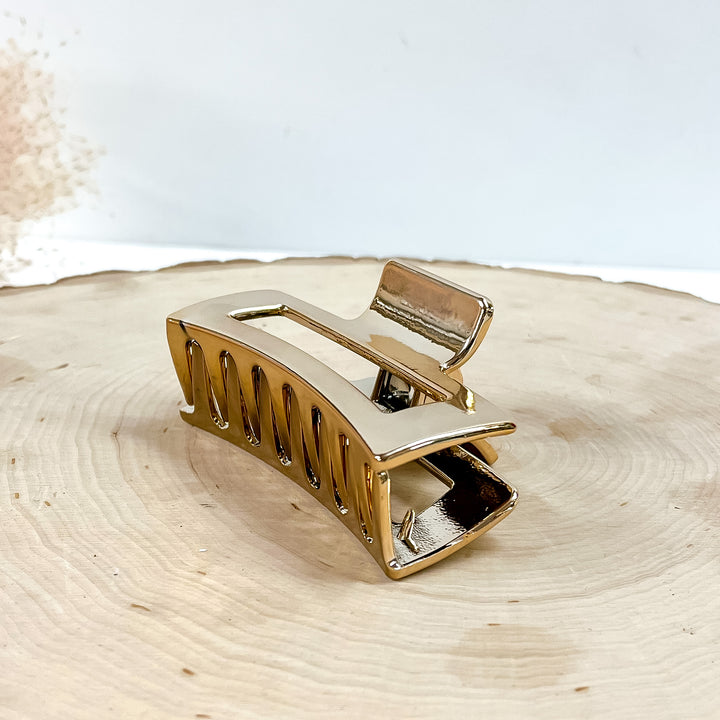 This is a rectangle metallic hair clip in rose gold/copper,  this clip is taken on a  slab of wood and in white background with a plant in the side as decor.