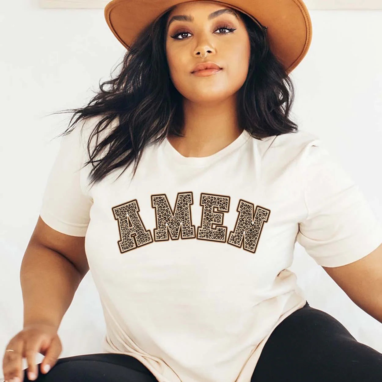 A cream colored short sleeve crew neck tee with the word "Amen" in a bold text and each letter is filled with a leopard print. Item is pictured on a plain white background