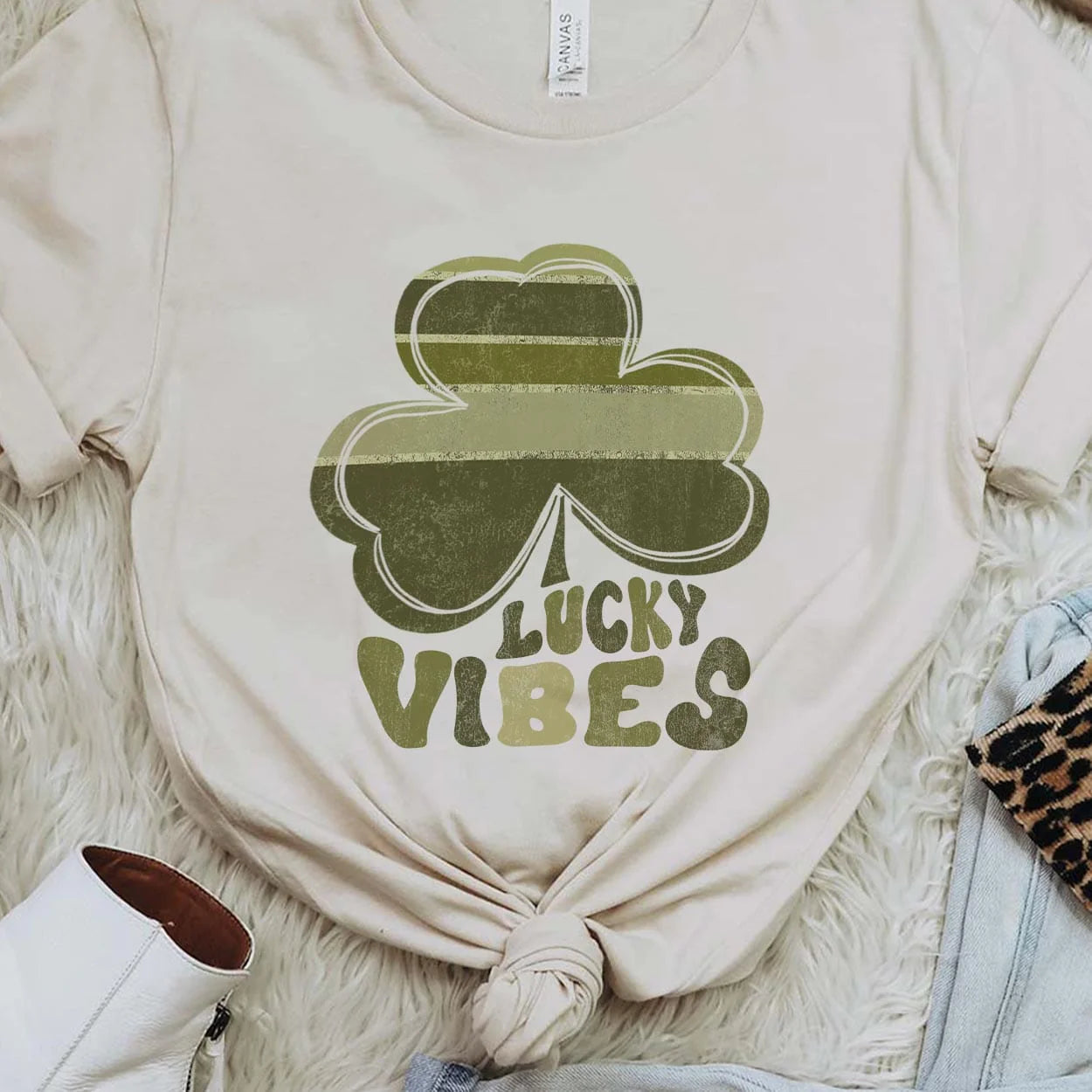 A cream crew neck sweatshirt featuring a large graphic of a clover with various shades of green and the words "lucky vibes" below it with each letter coordinating to a color in the clover. Item is pictured on a white background.