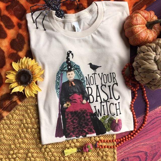 A cream colored graphic tee that states not your basic witch. There is a witch with a crow, broom, and cat along with two pumpkins. 